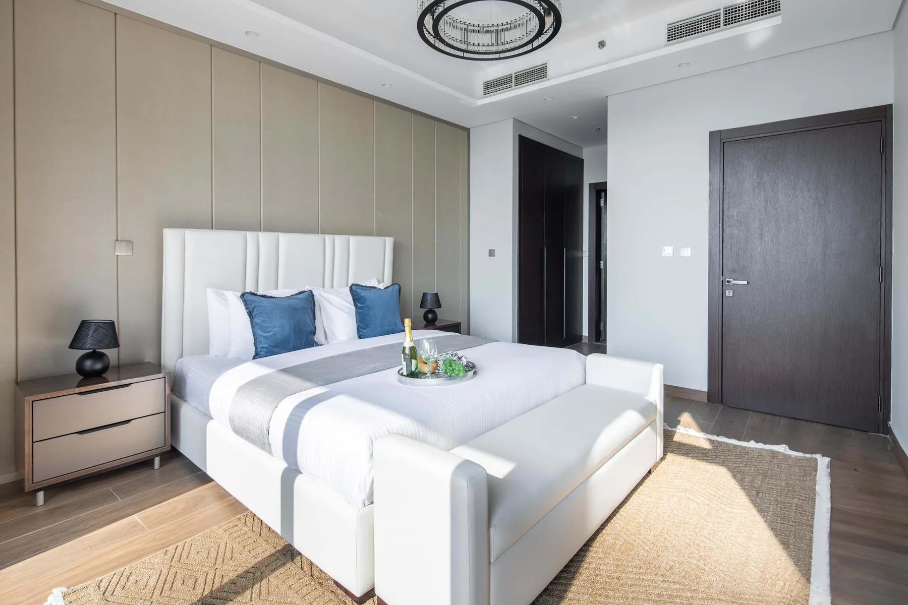A bright bedroom with a large bed, bedside tables, and a woven rug.