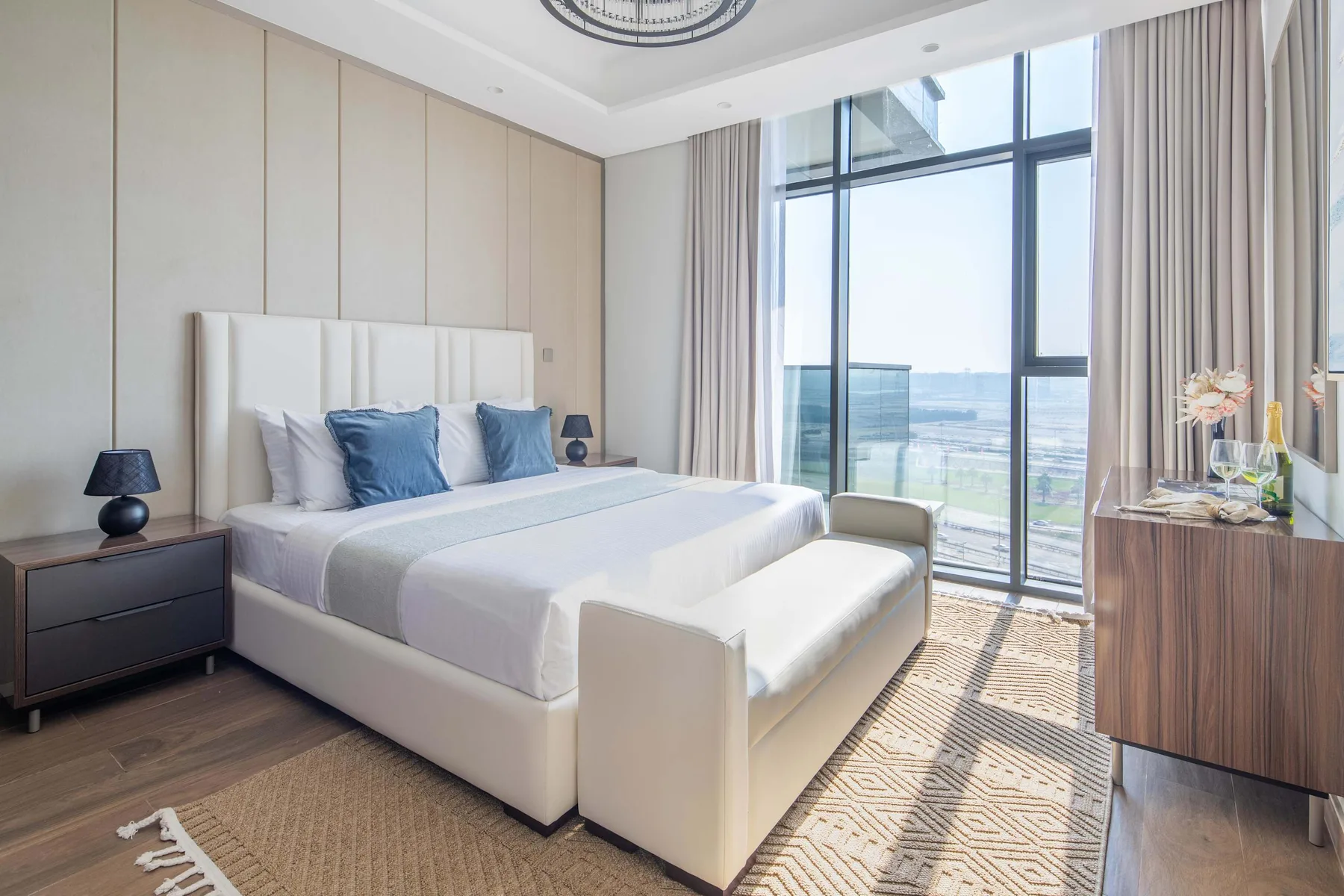 A bright bedroom with a large bed, bedside tables, and floor-to-ceiling windows.