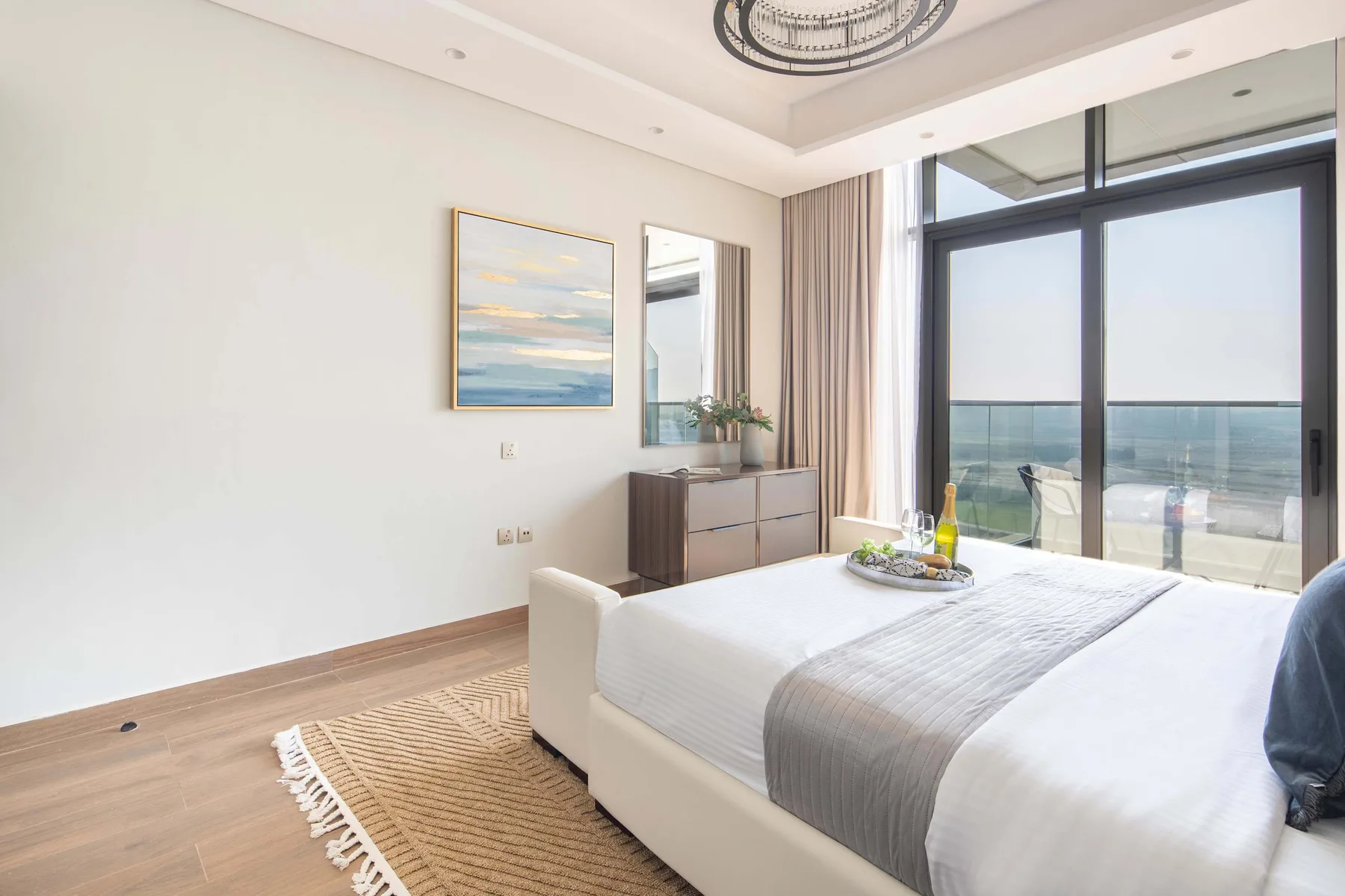 A bright bedroom with a neatly made bed beside large windows overlooking the water.