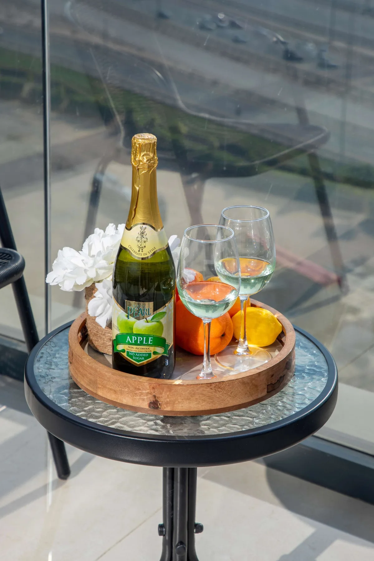 A small round table holds a bottle of sparkling drink, glasses, and fruit.