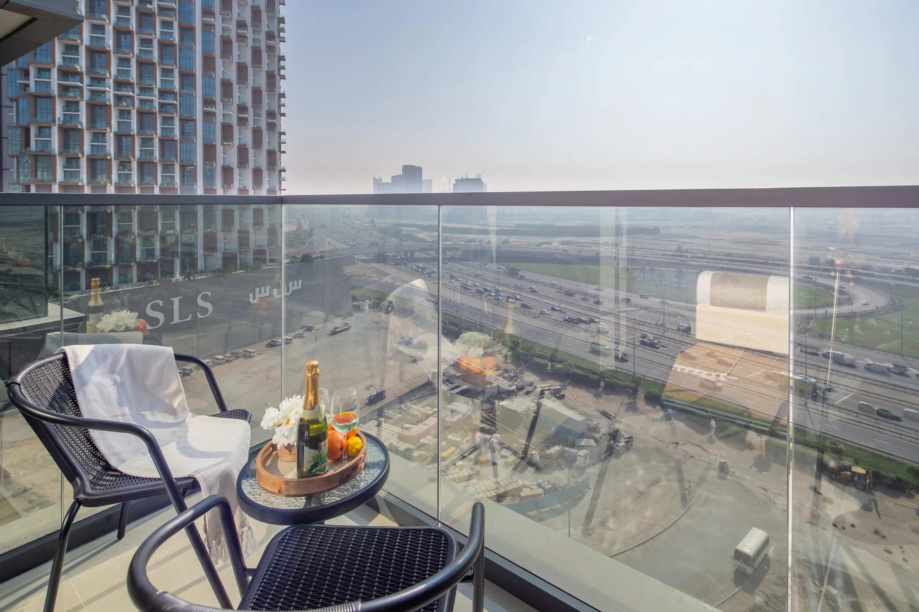 A balcony seating area overlooks a city roadway through a glass railing.