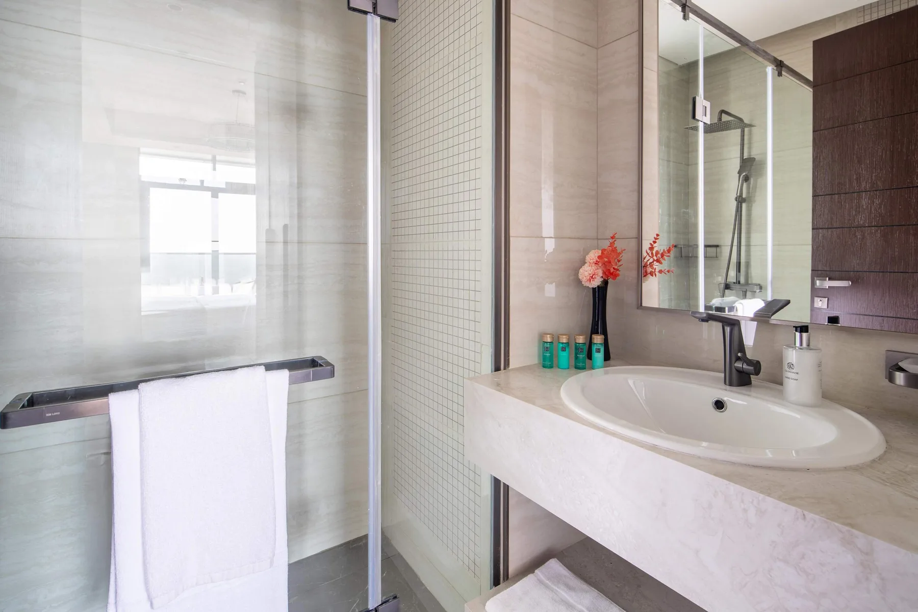 A bright bathroom has a glass shower, a sink, and a white towel.
