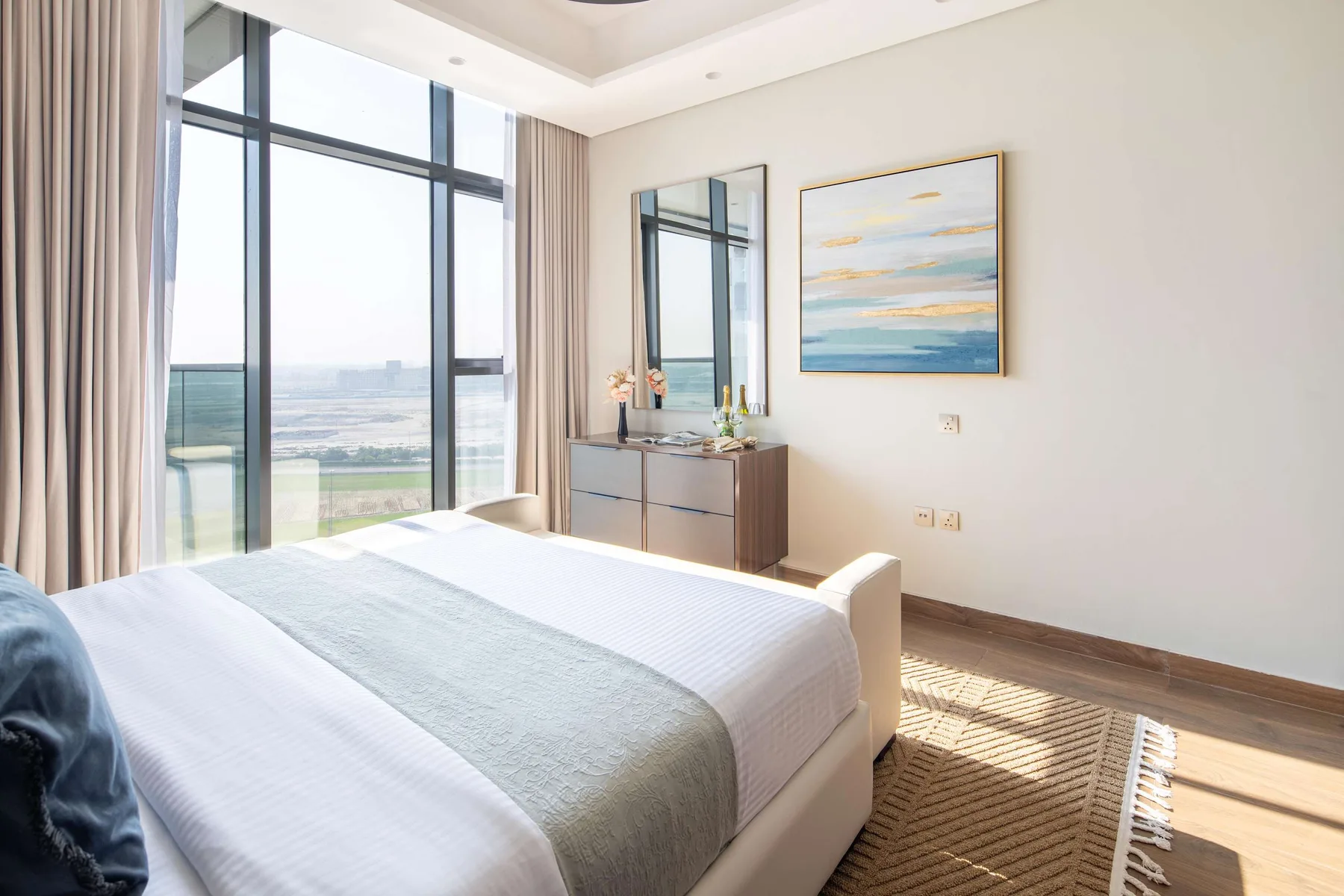 A bright bedroom with a neatly made bed beside large windows overlooking the water.