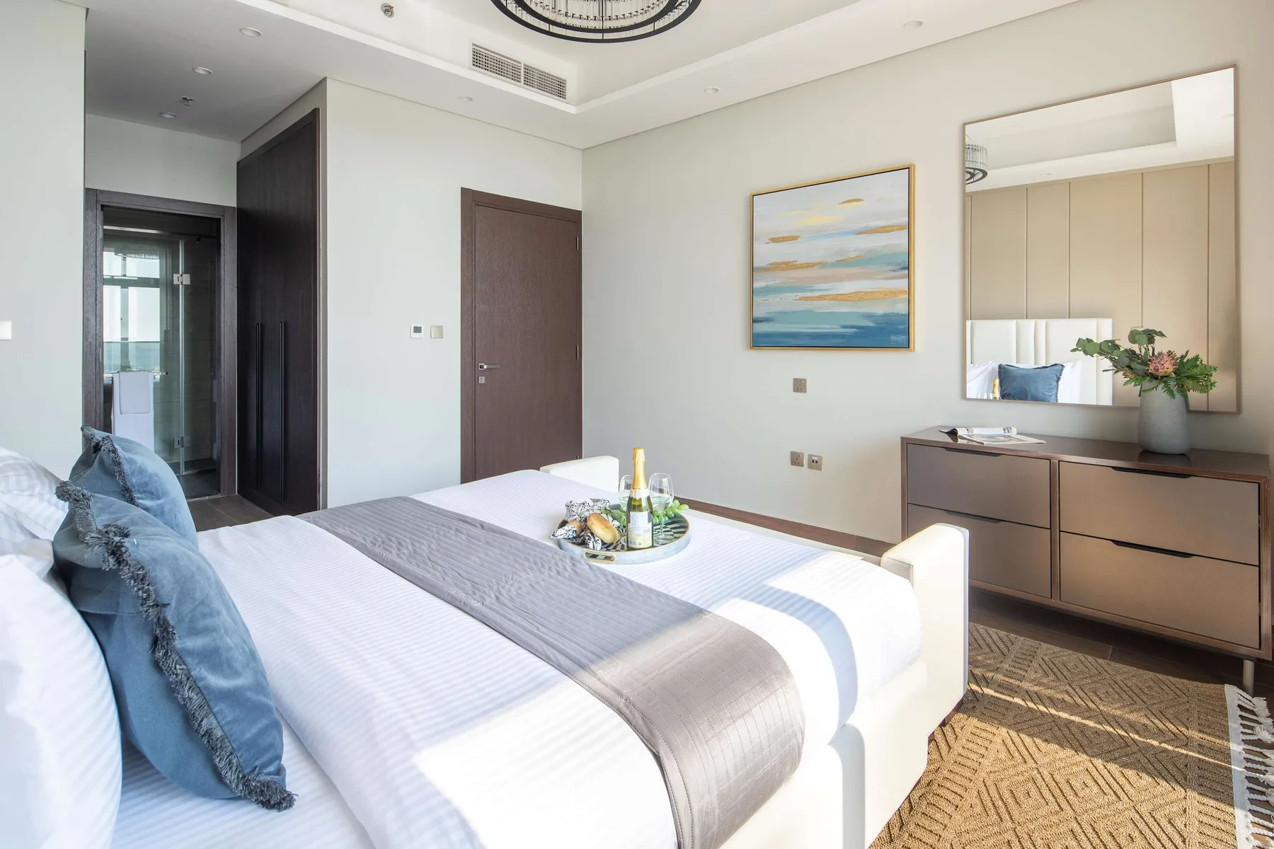 A bright bedroom with a neatly made bed and a framed landscape painting.