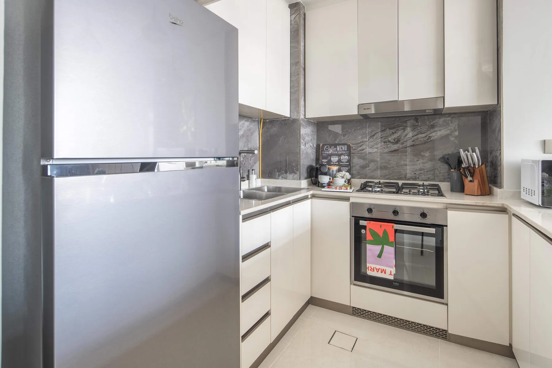 A bright kitchen with white cabinets, a refrigerator, and a built-in oven.