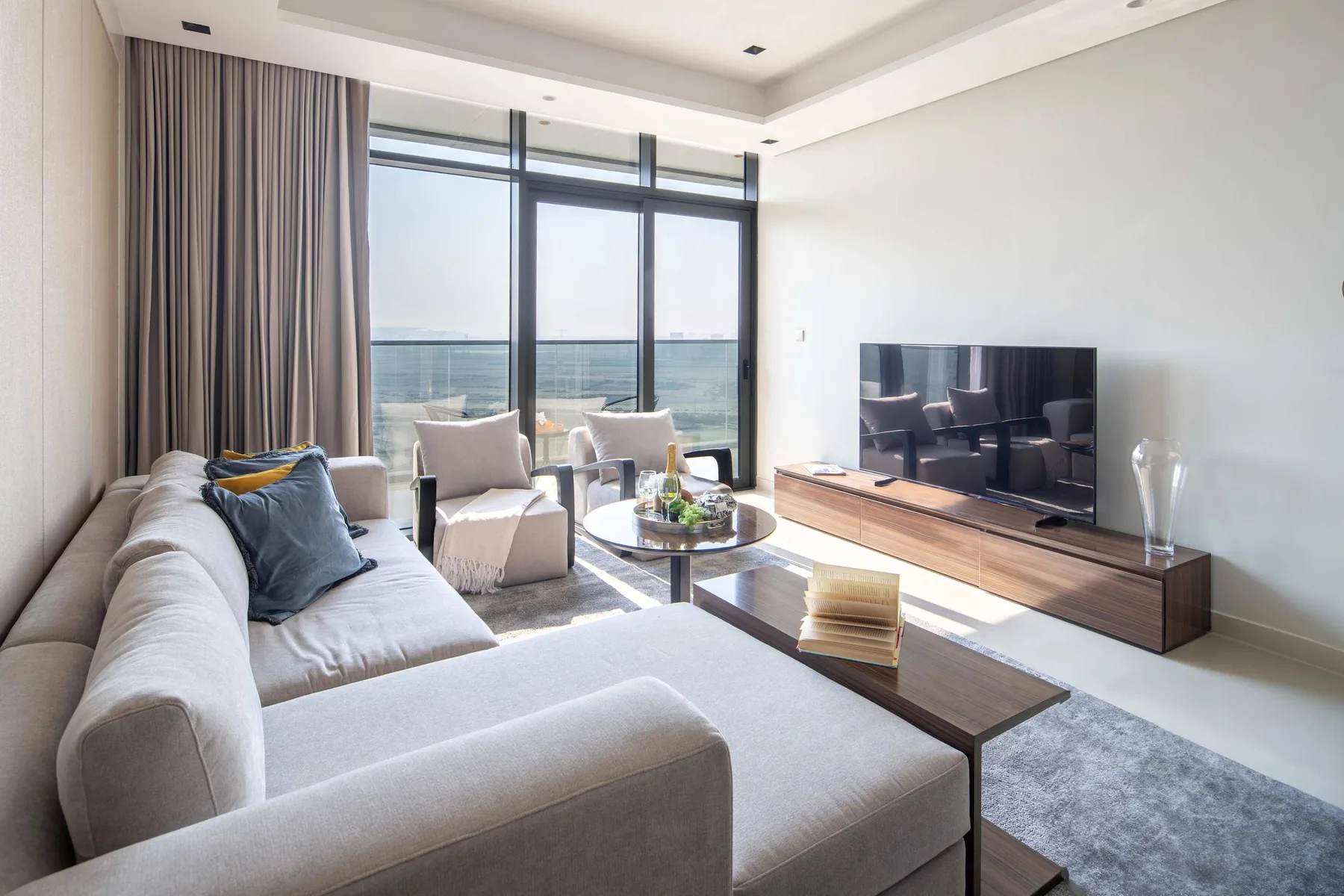 Una sala luminosa con asientos, un televisor y vistas al mar por grandes ventanales.