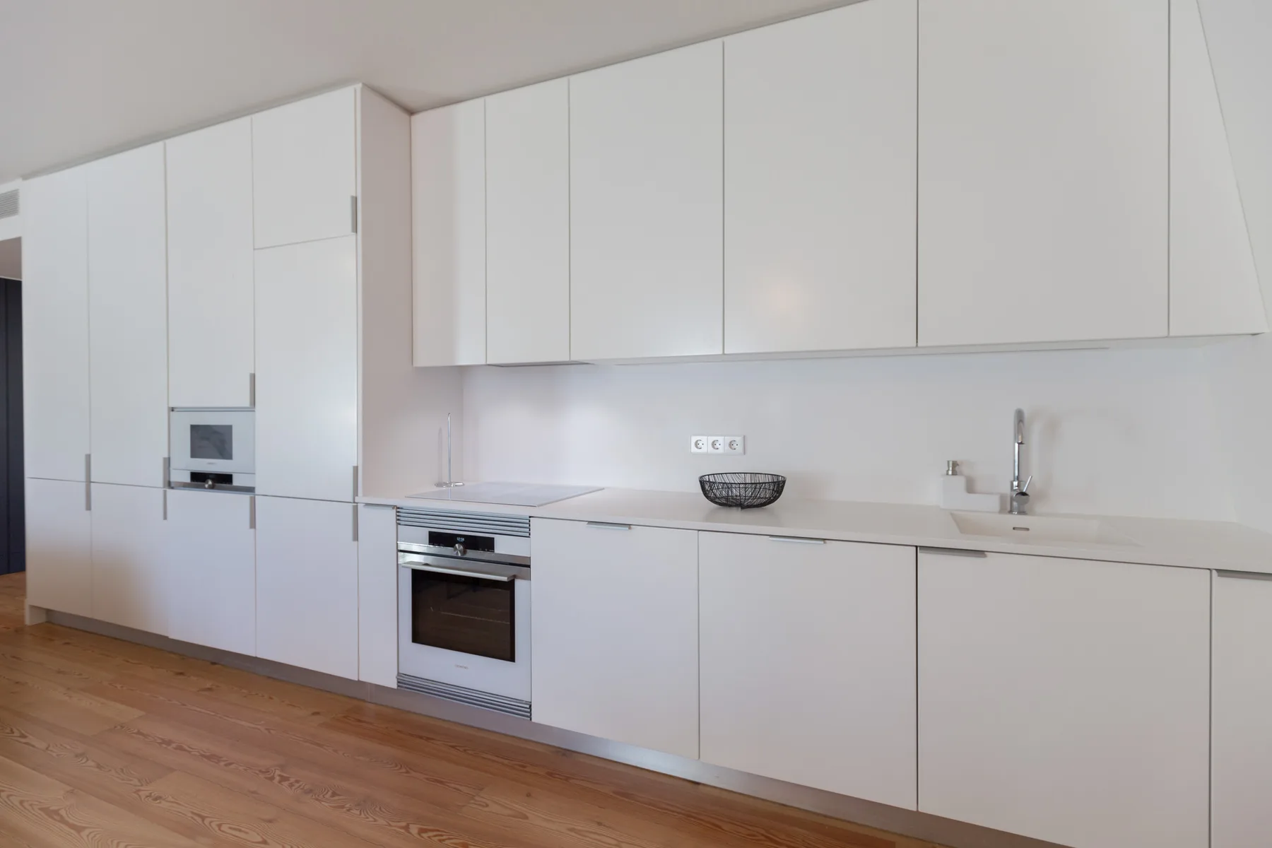 A modern kitchen with white cabinetry and a wooden floor.