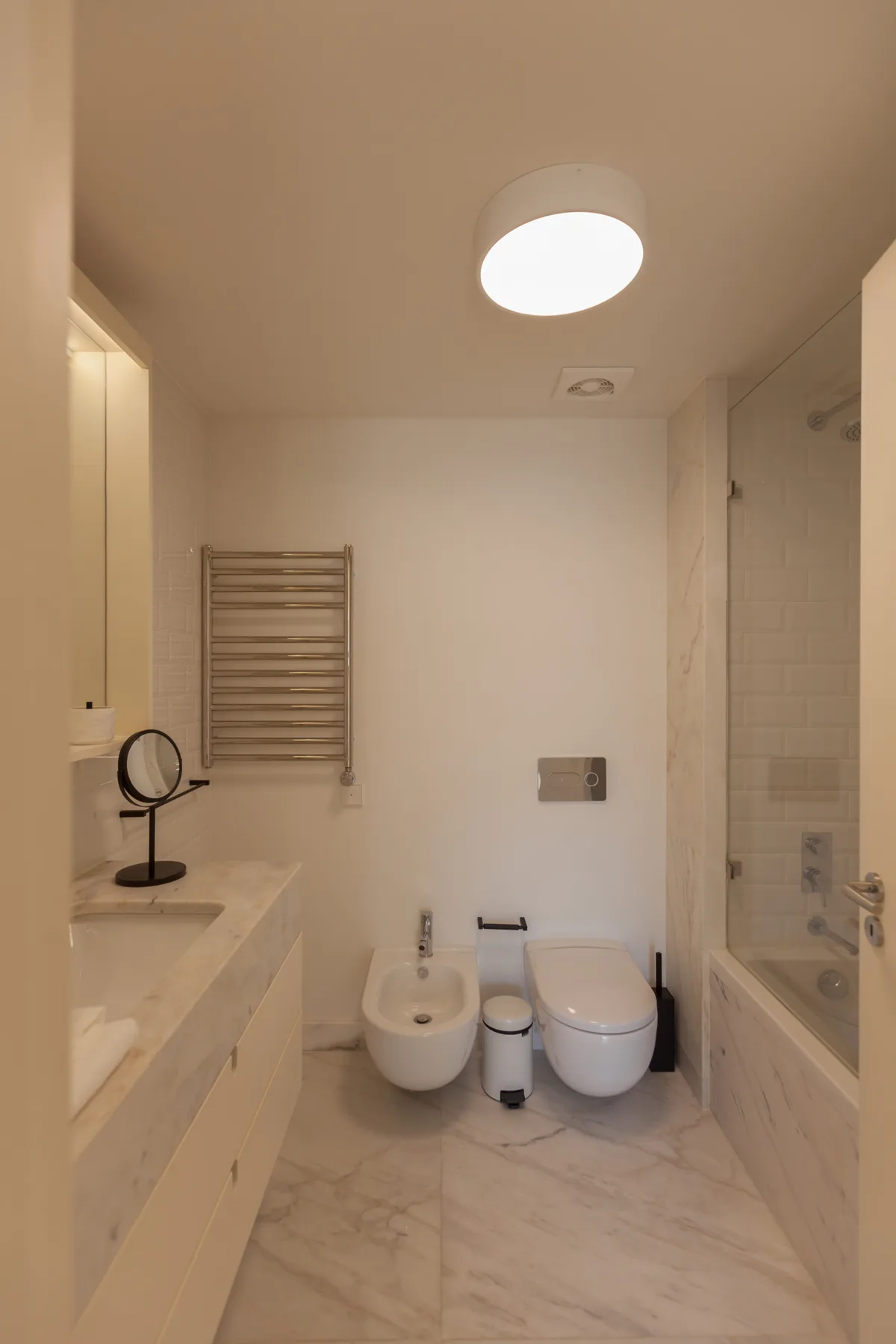 A bathroom with a sink, wall-mounted towel warmer, and shower.