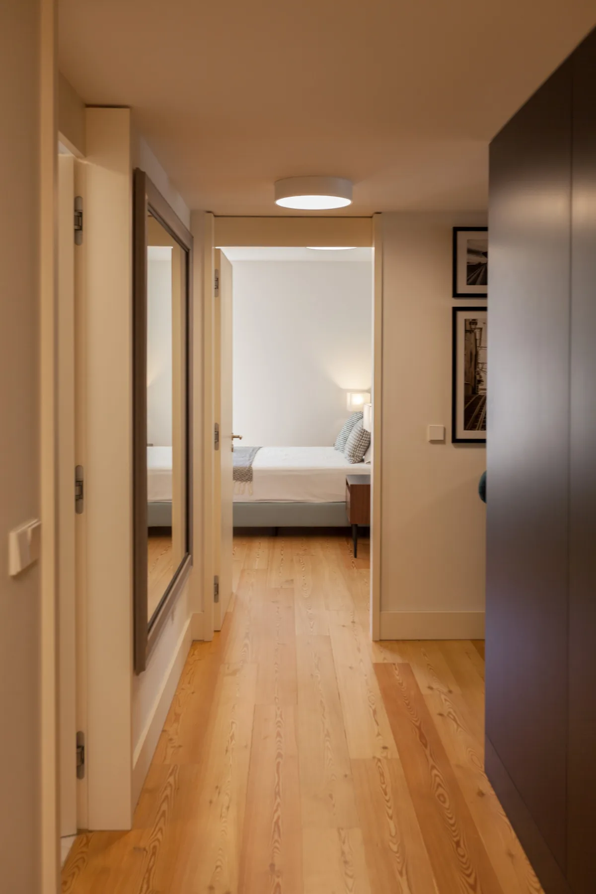 A hallway with light wood flooring leads to a bedroom.