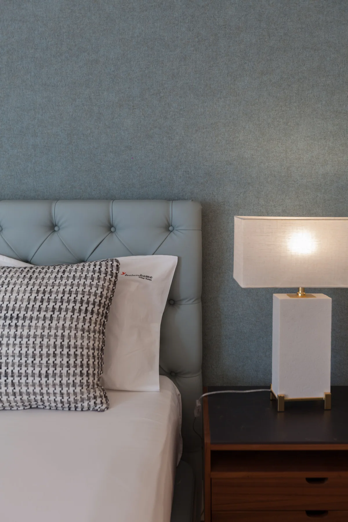 A bedroom with a bed and a lit lamp on a bedside table.