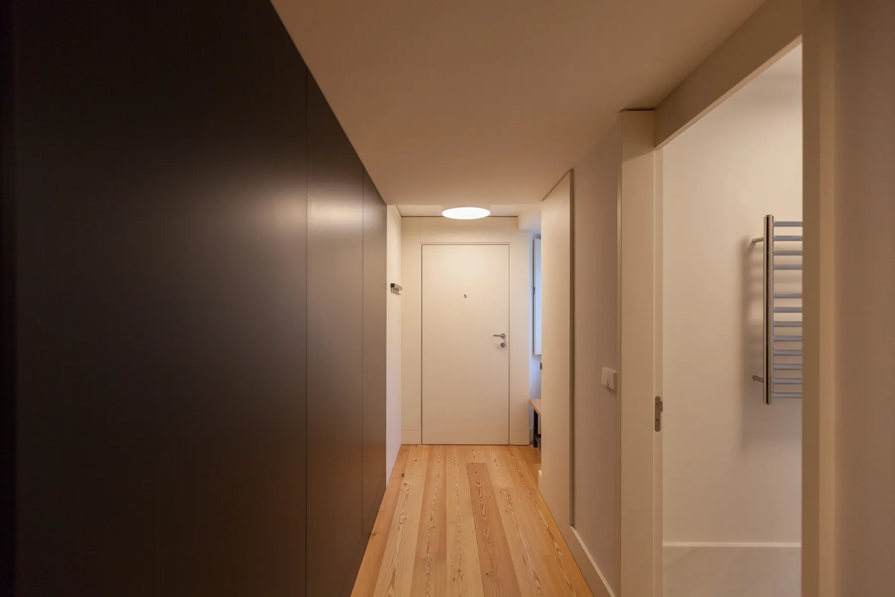 A hallway with wood flooring leads to a closed door.