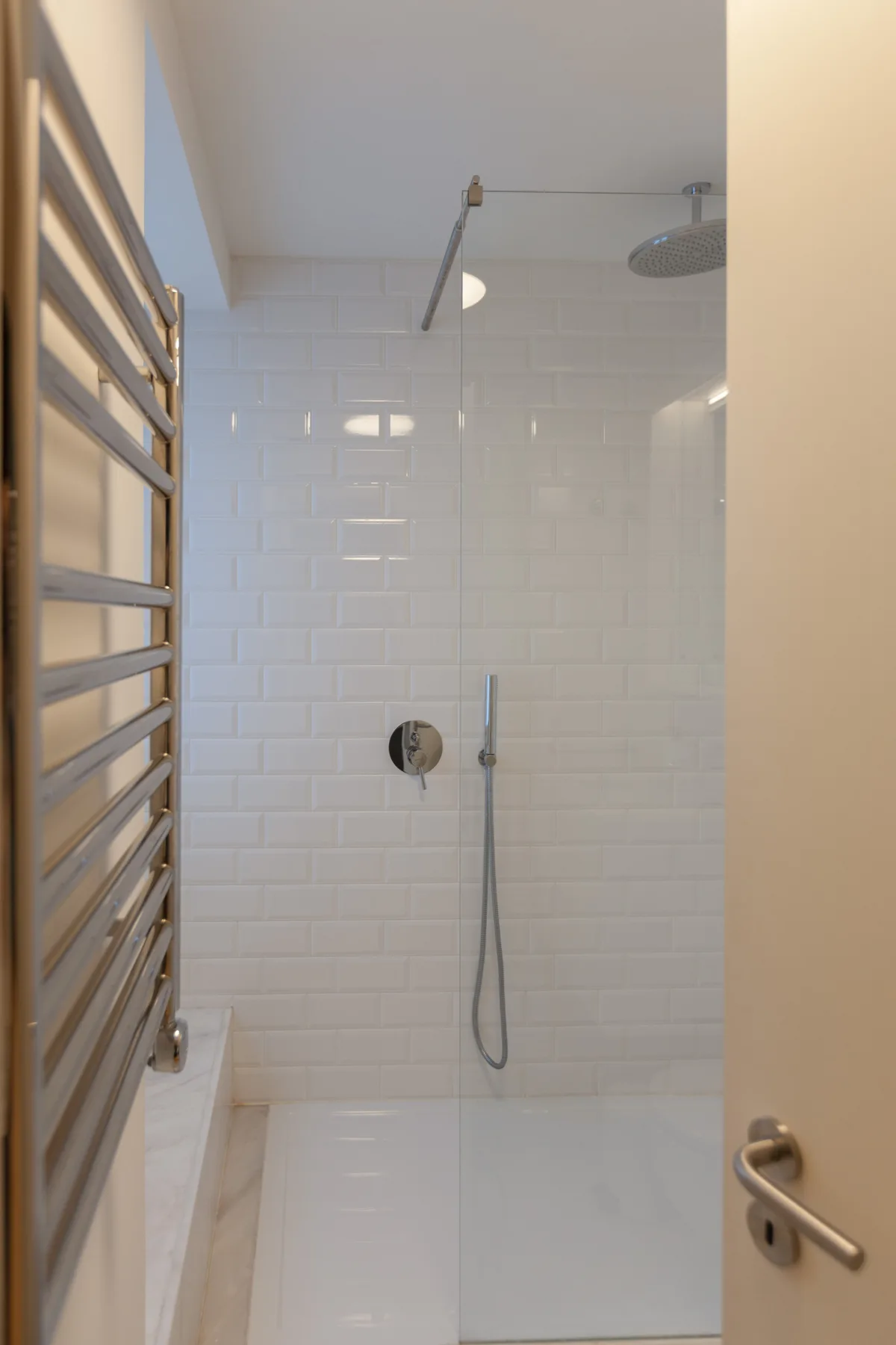 A tiled shower area with a wall-mounted showerhead and handheld sprayer.