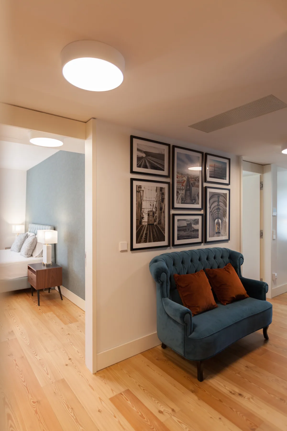 An interior hallway features a blue upholstered seating area beneath framed pictures.