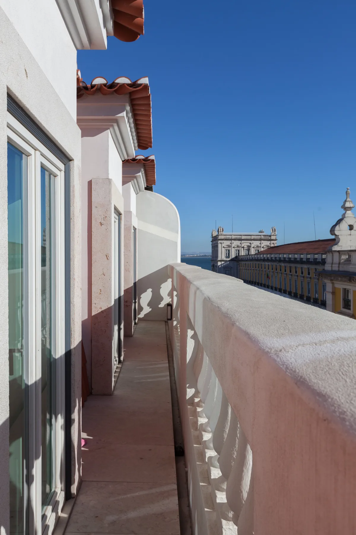 A narrow balcony overlooks neighboring rooftops beneath a clear blue sky.