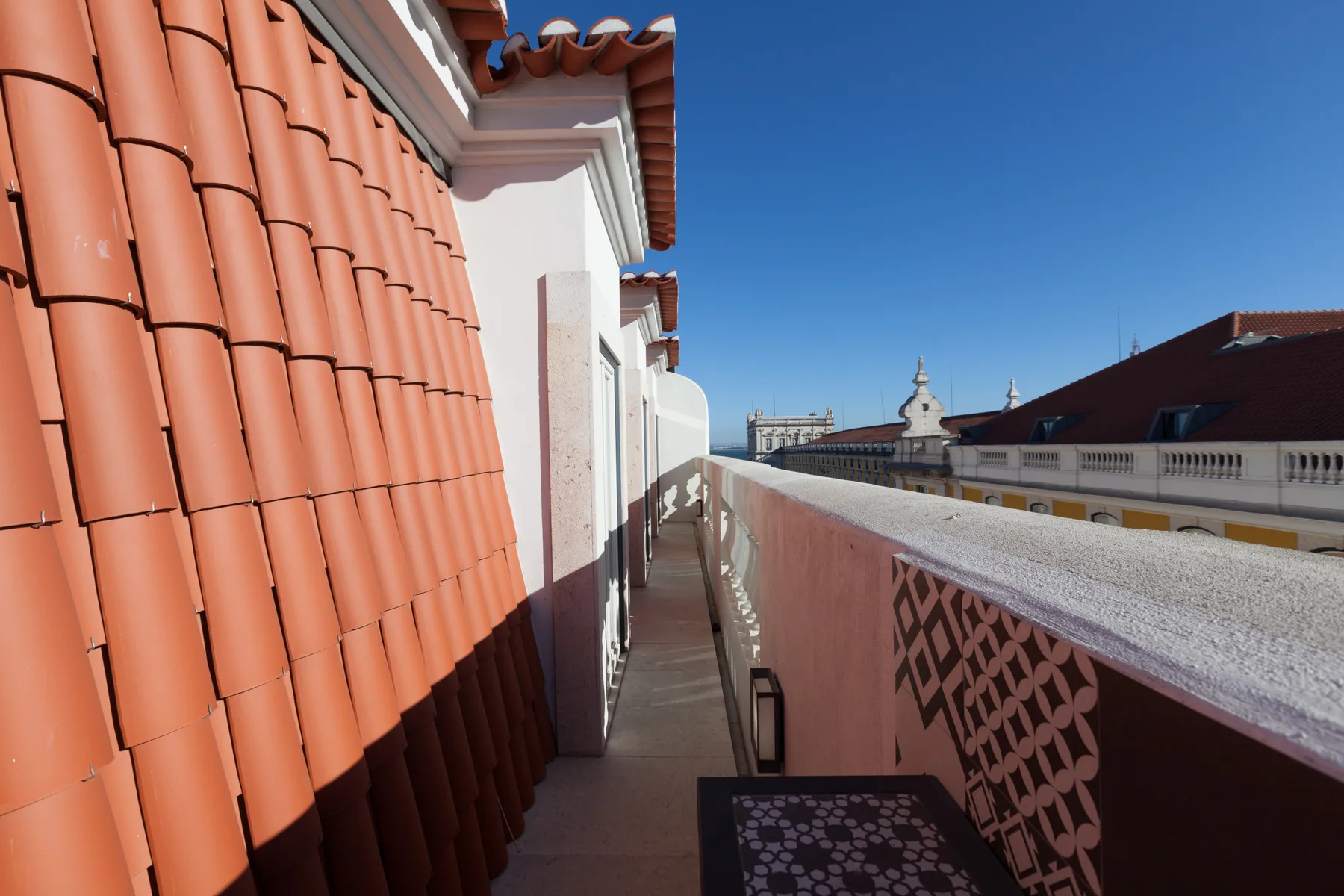 A narrow outdoor balcony walkway runs beside a tiled roof, overlooking nearby rooftops.