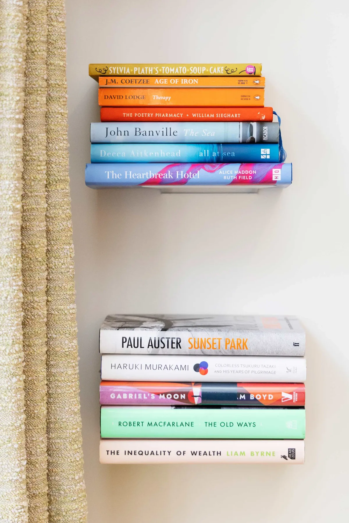 Hay libros colocados en dos estantes de pared junto a una cortina.