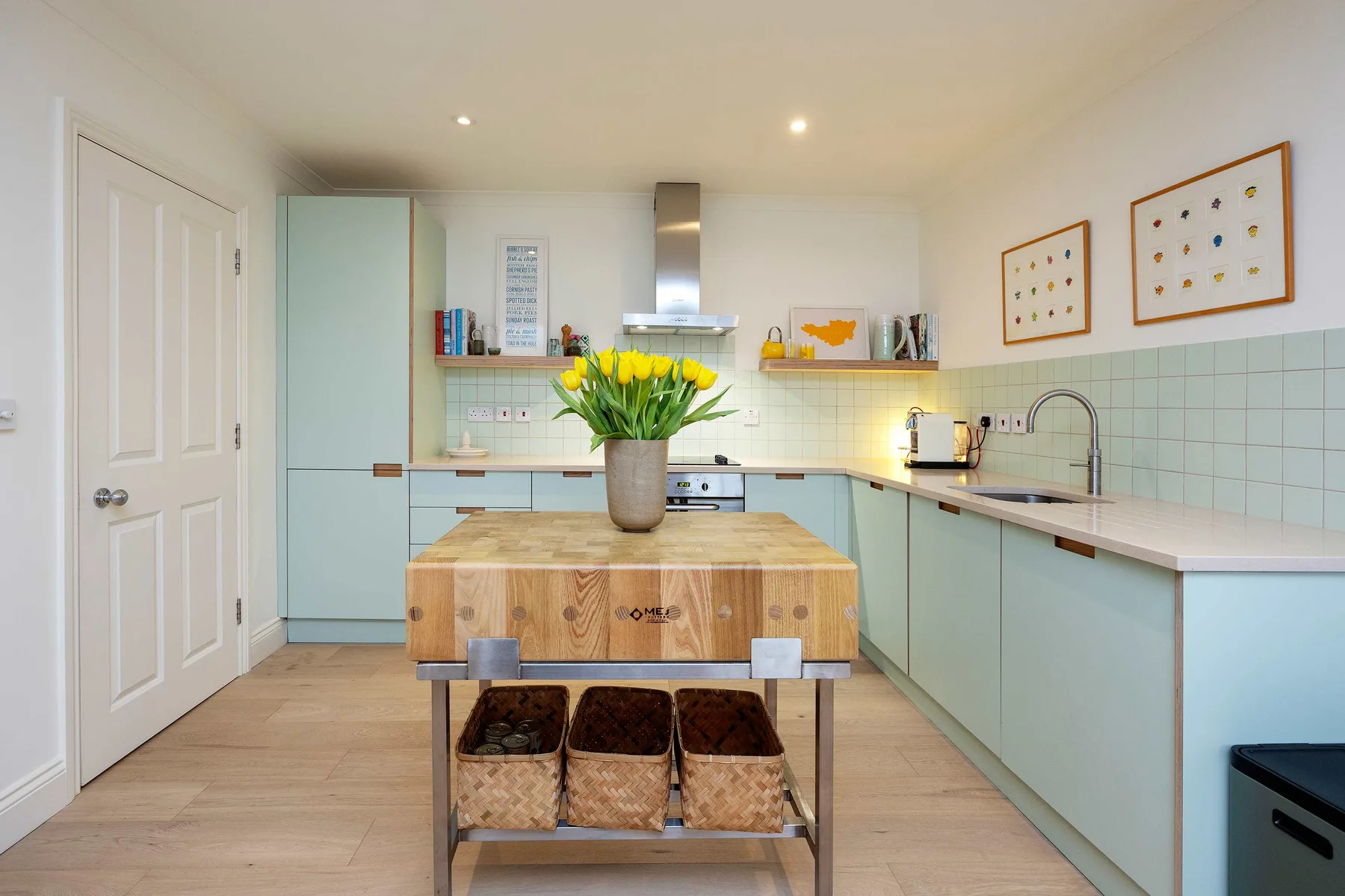 Una cocina luminosa con gabinetes azul claro, una isla central y flores amarillas.