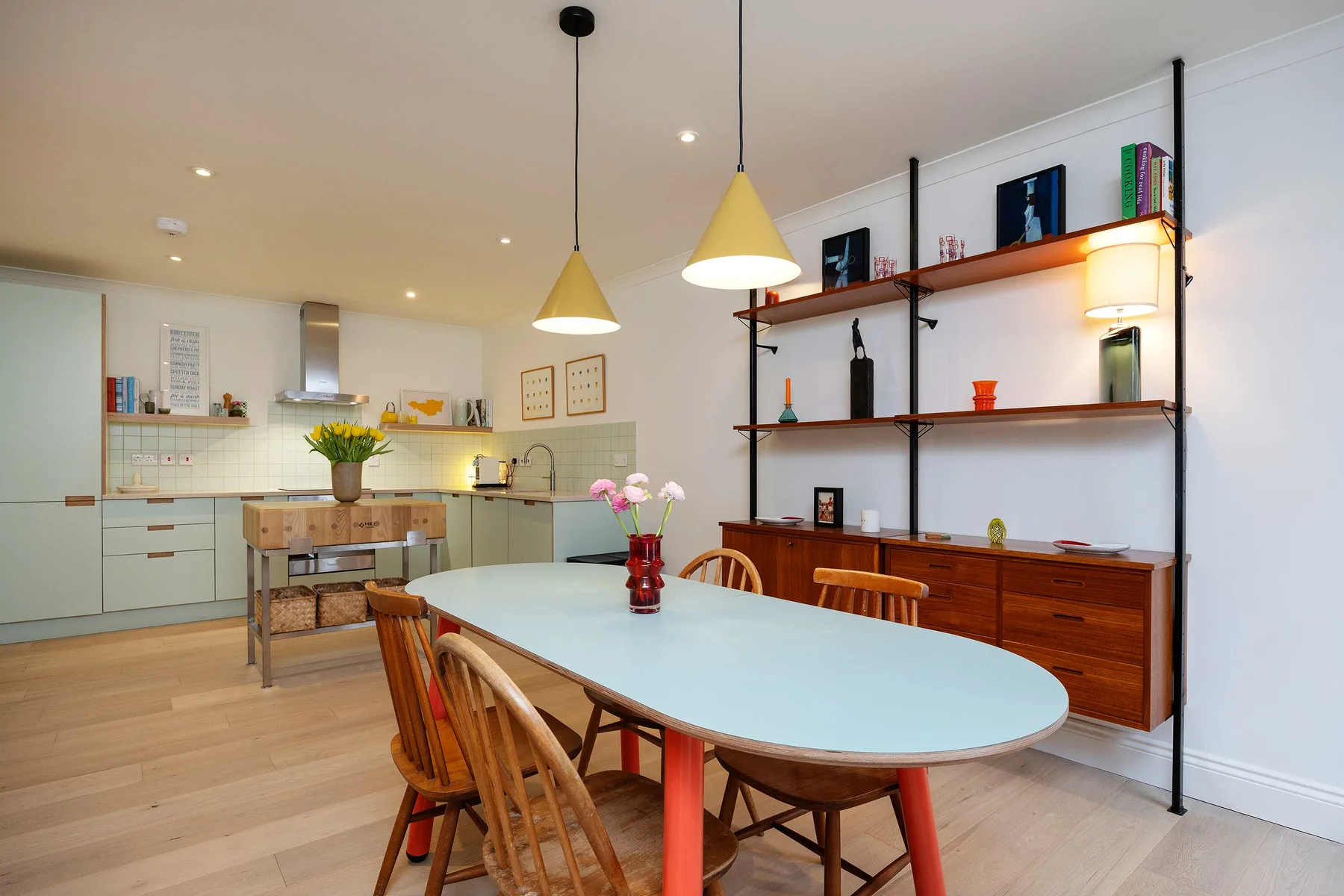 Una luminosa cocina-comedor con una mesa larga bajo lámparas colgantes.