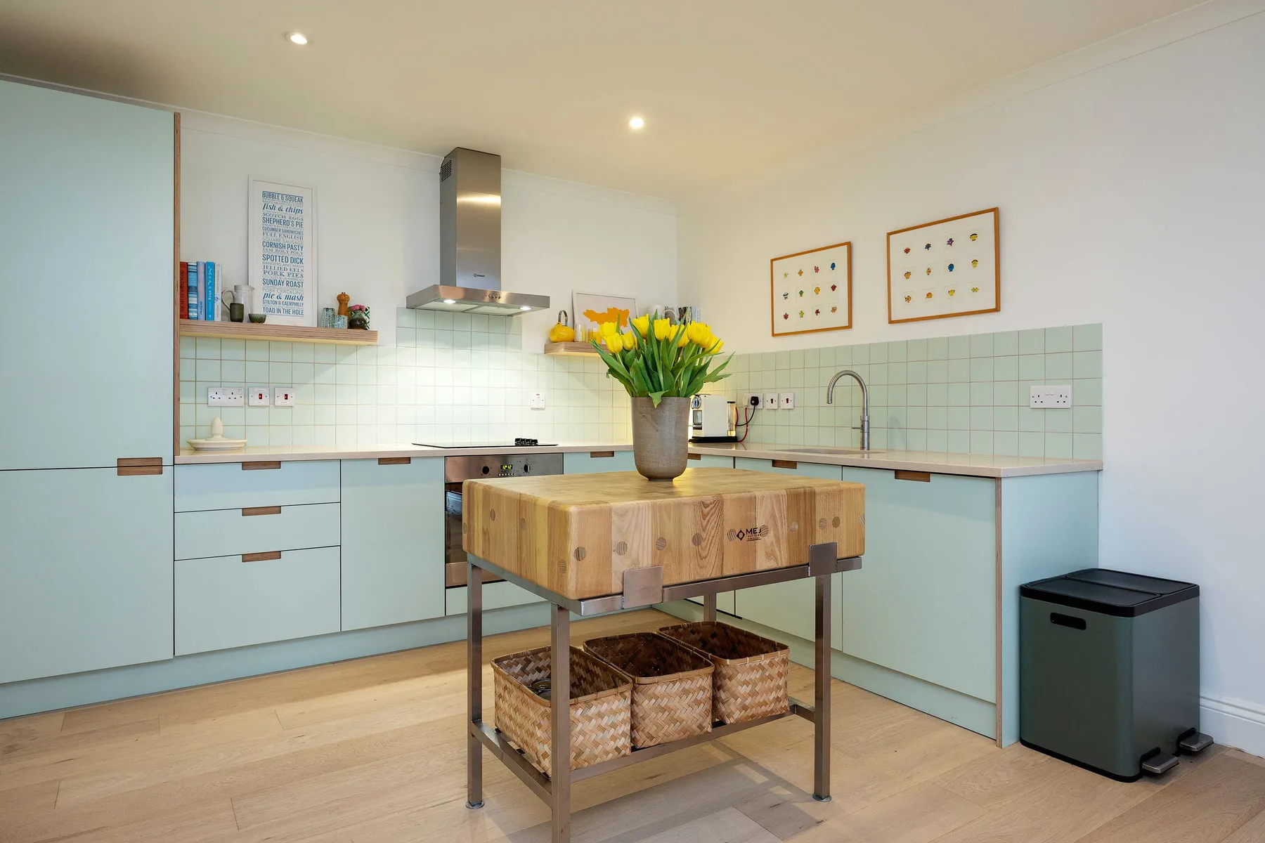 A bright kitchen with pale cabinets, a central island, and flowers on the countertop.