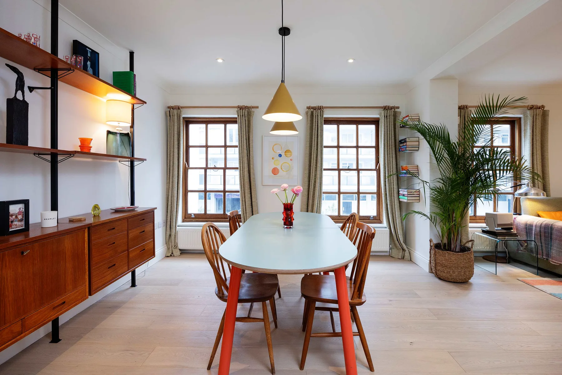 A dining room with a long table, wooden seating, and tall windows.