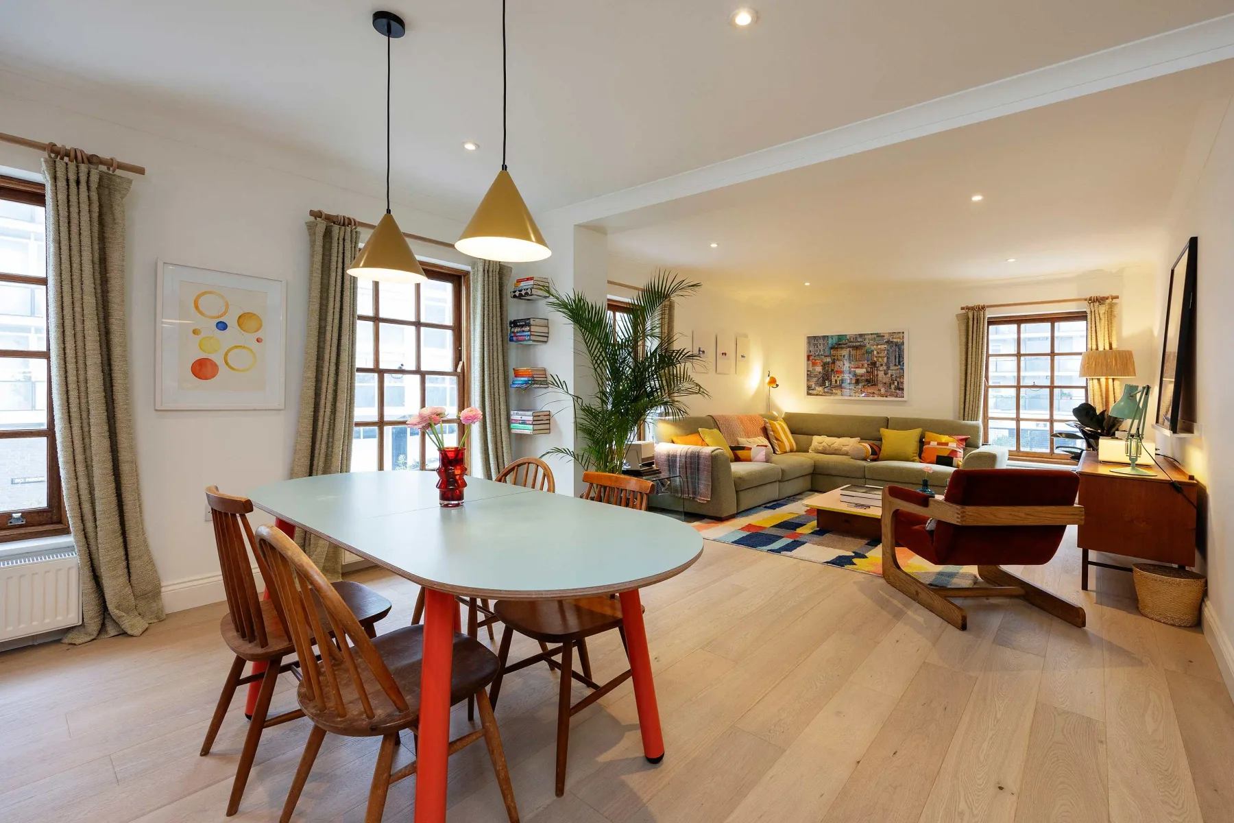 El comedor se abre a una sala de estar con un sofá seccional y ventanas grandes.