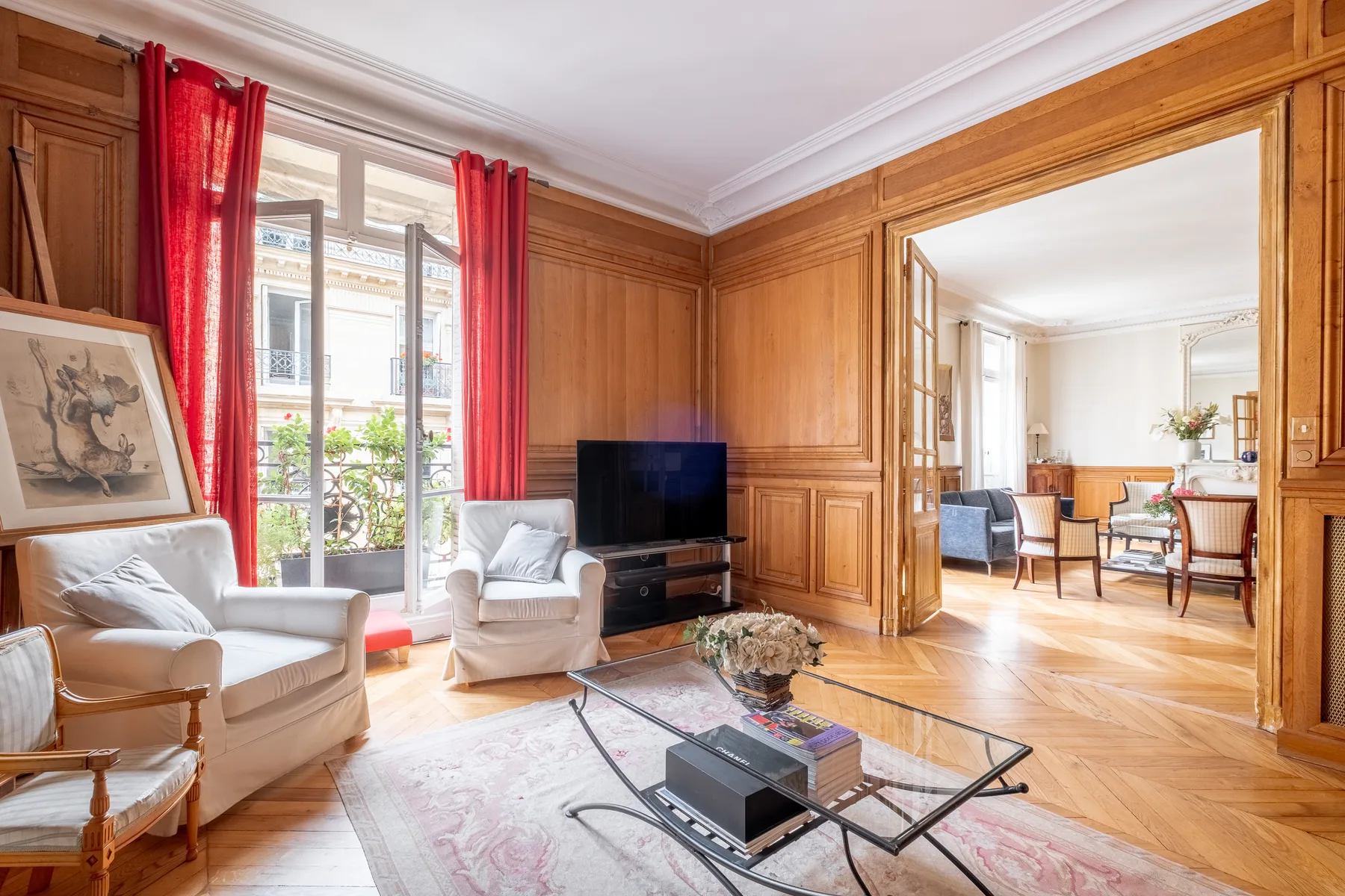 A wood-paneled living room with seating, a television, and tall windows.