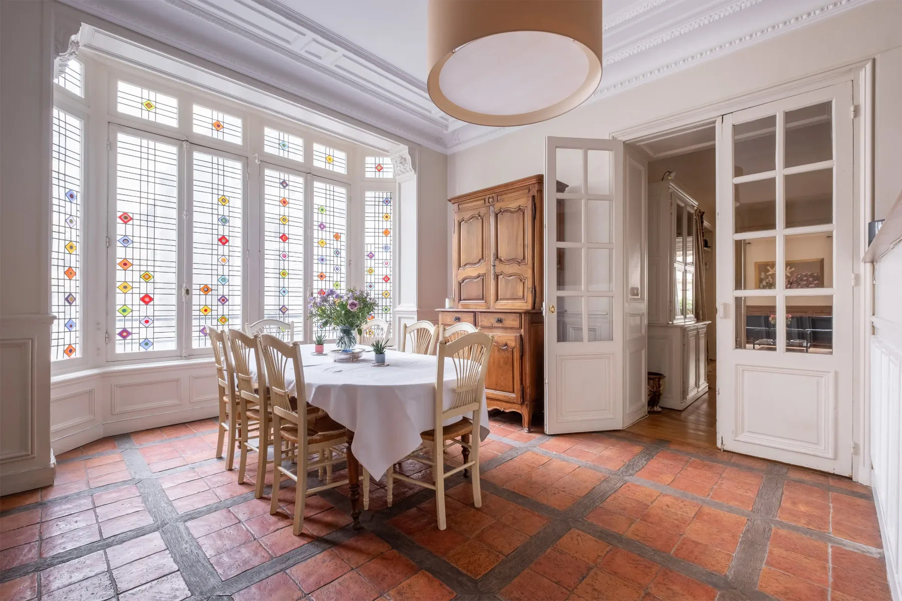 A dining room with a table and chairs beside tall decorative windows.
