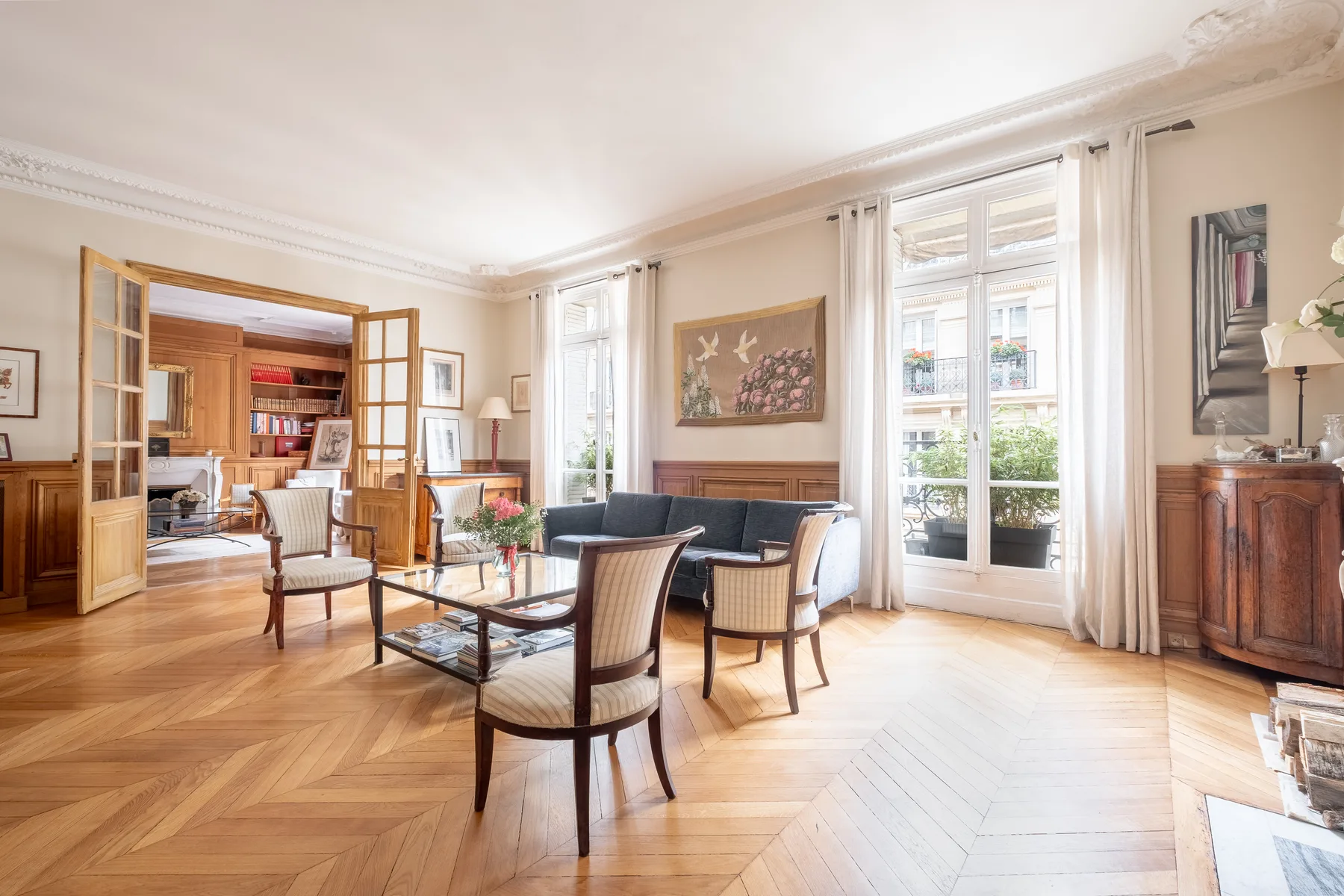 A bright living room with seating around a glass coffee table and tall windows.