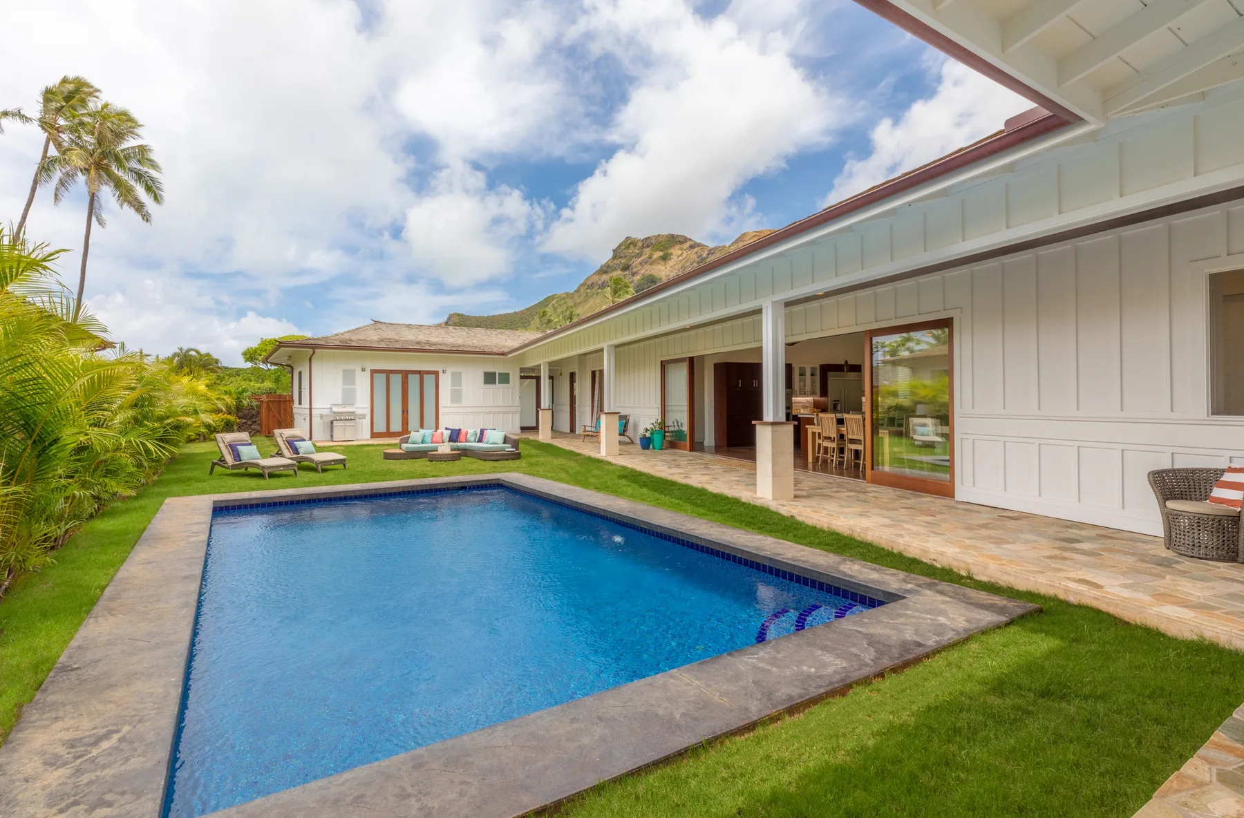 A backyard pool beside a covered patio and a light-colored house.