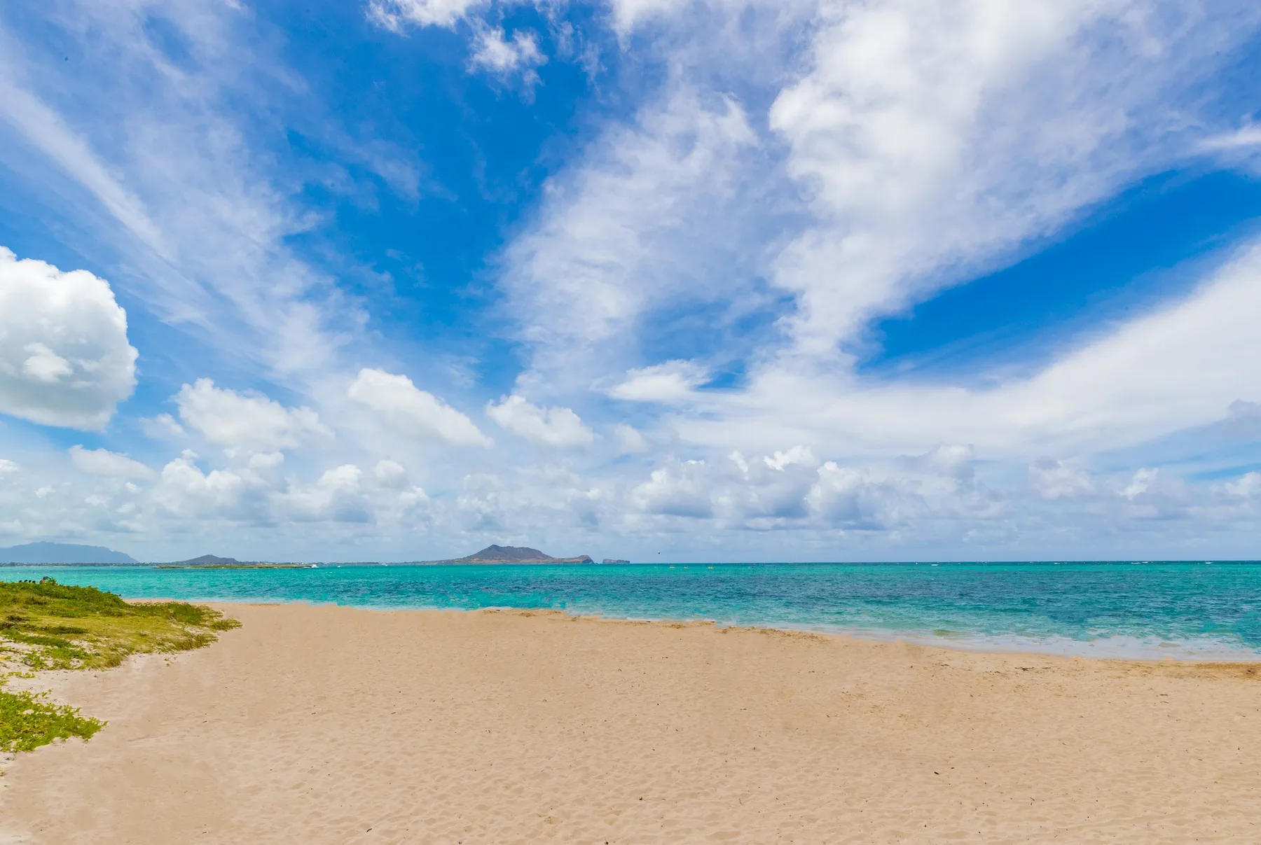 A sandy beach meets turquoise water beneath a cloudy blue sky.