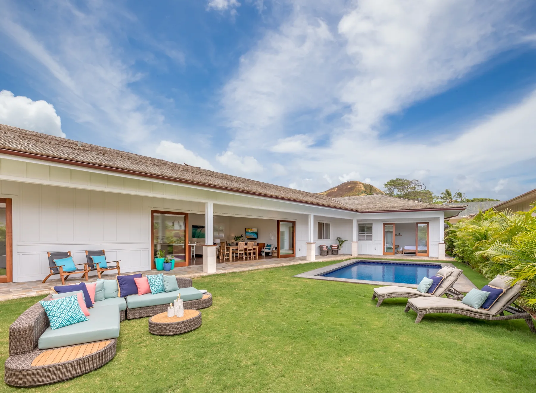 A single-story house opens onto a lawn with outdoor seating and a swimming pool.