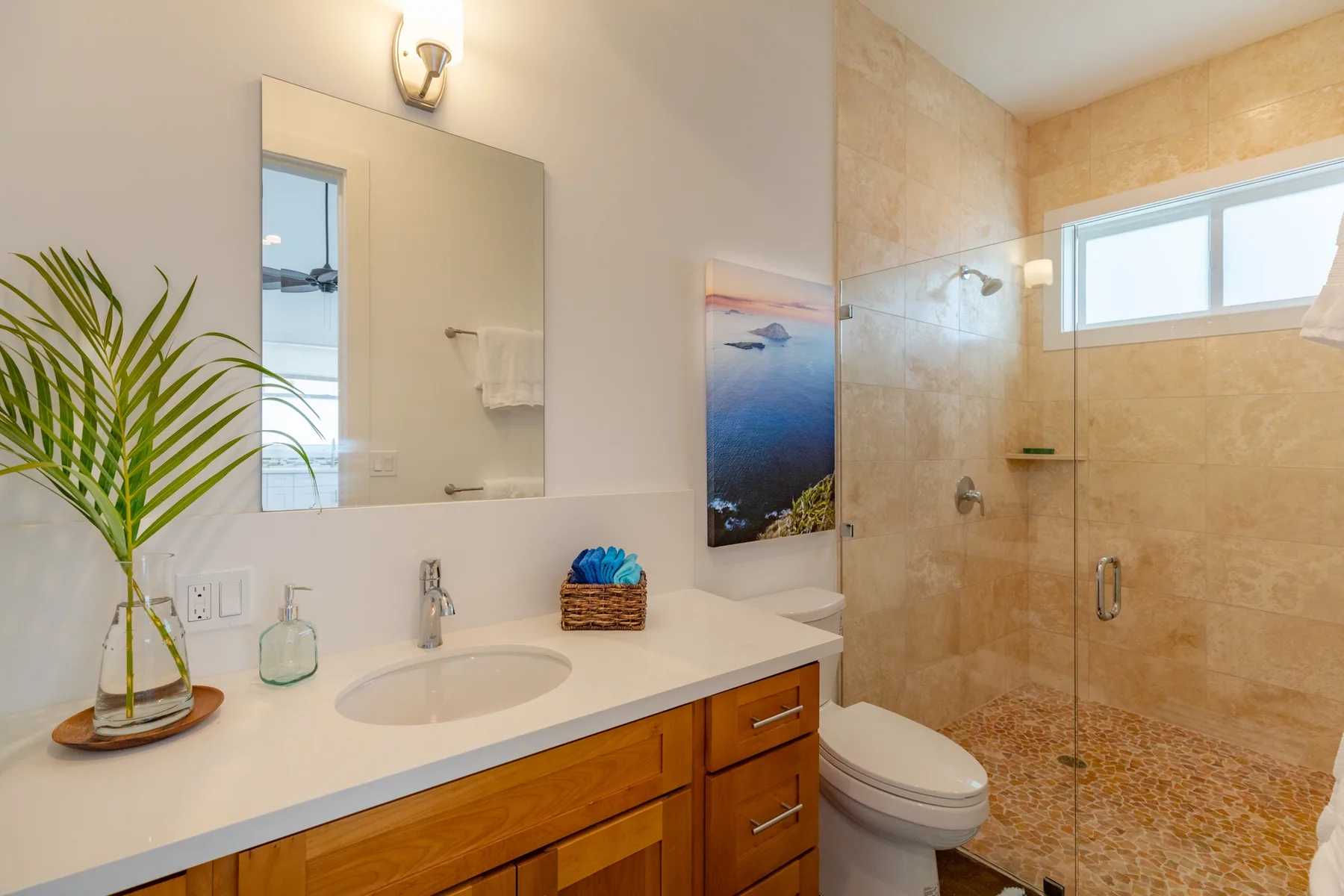 A bright bathroom with a vanity, toilet, and glass shower.