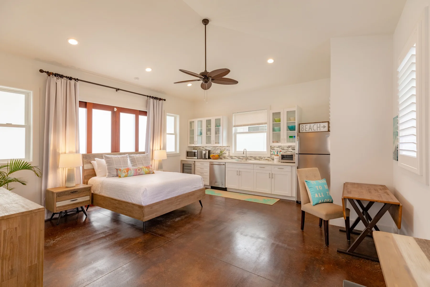 A bright bedroom with a bed, kitchen cabinets, and a refrigerator.