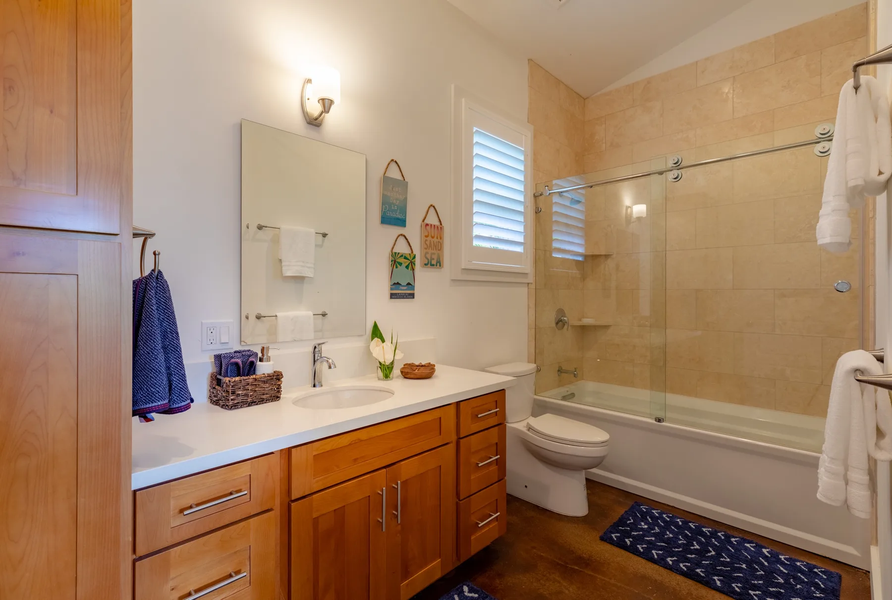A bathroom with a vanity, mirror, toilet, and bathtub with a glass screen.