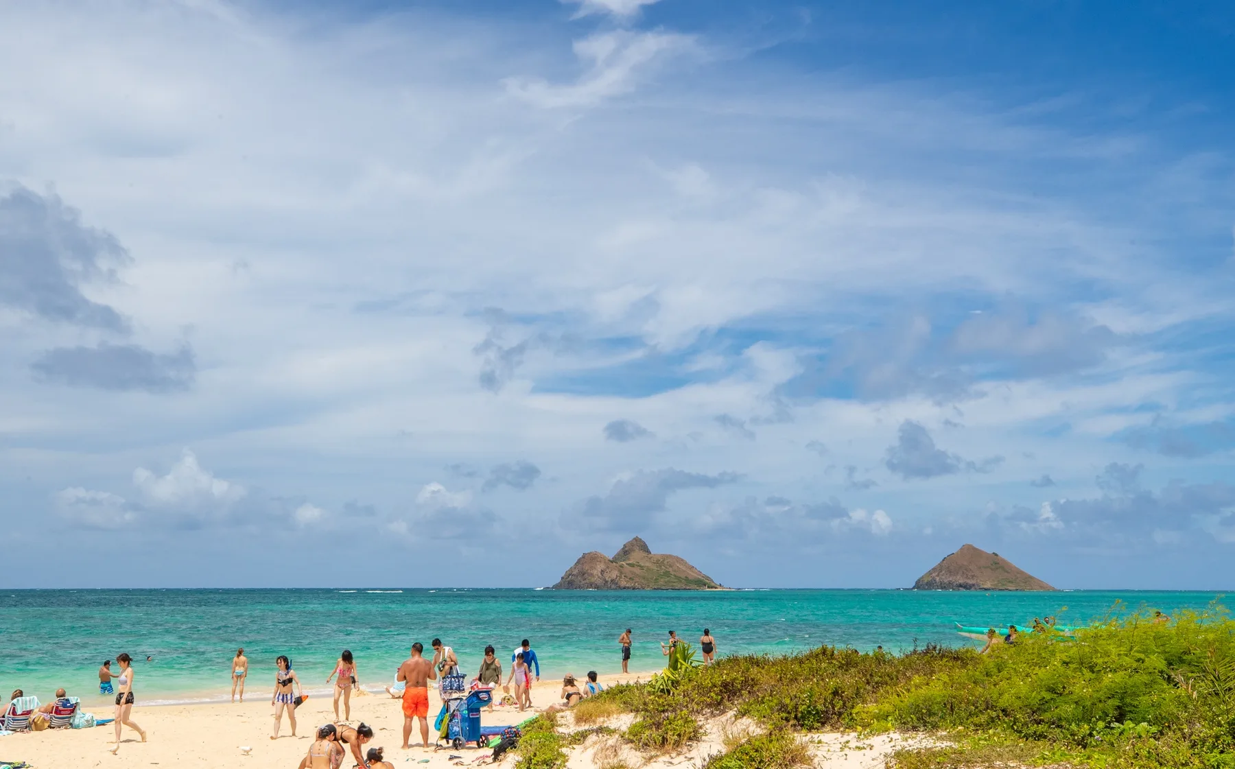 A sandy beach with people along the shore and a small island offshore.