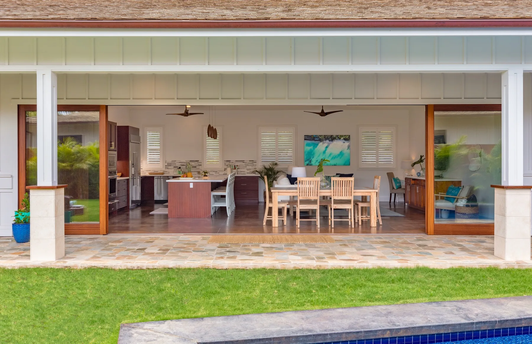 An open-sided patio dining area overlooks a green lawn, with a table and seating.