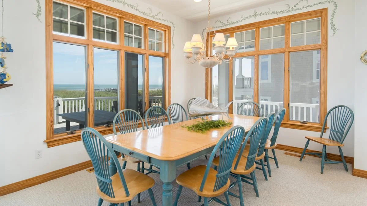 Un comedor luminoso con una mesa de madera, asientos azules y ventanas grandes.