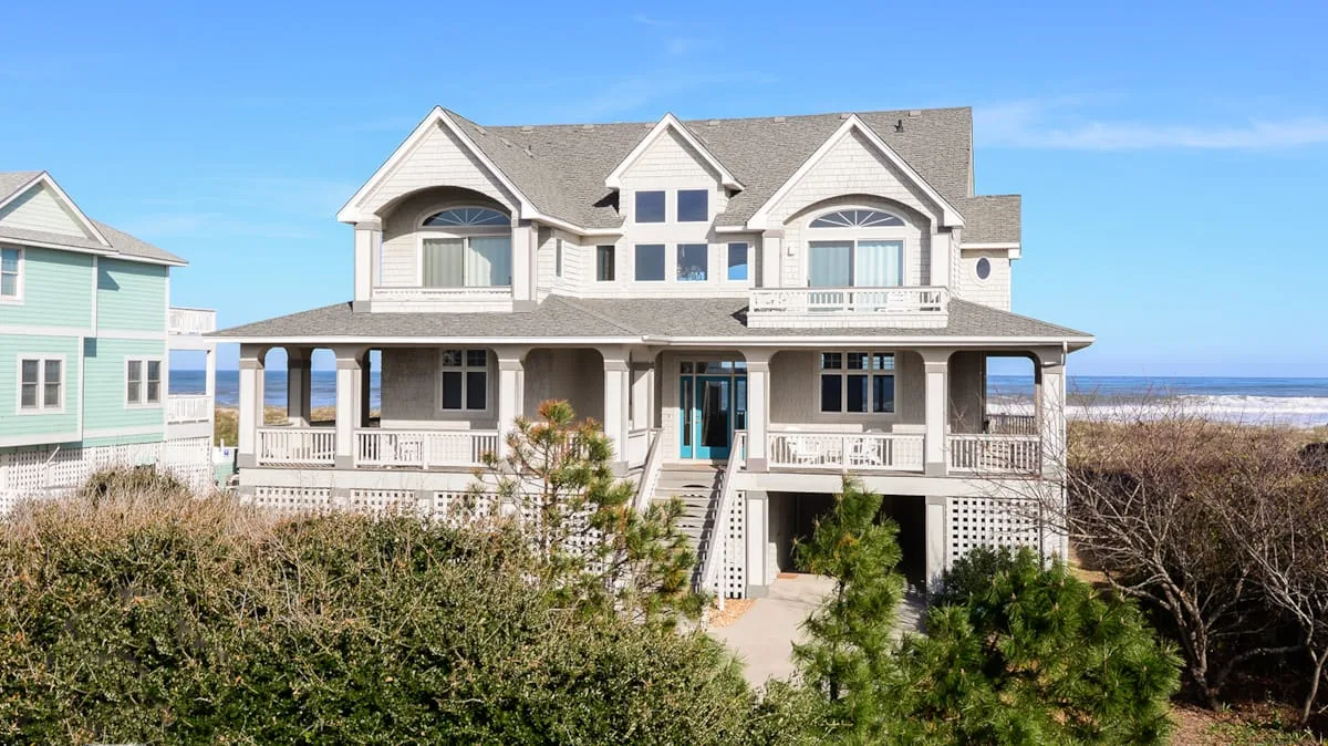 Una gran casa costera con balcones y un porche cubierto da a la playa.