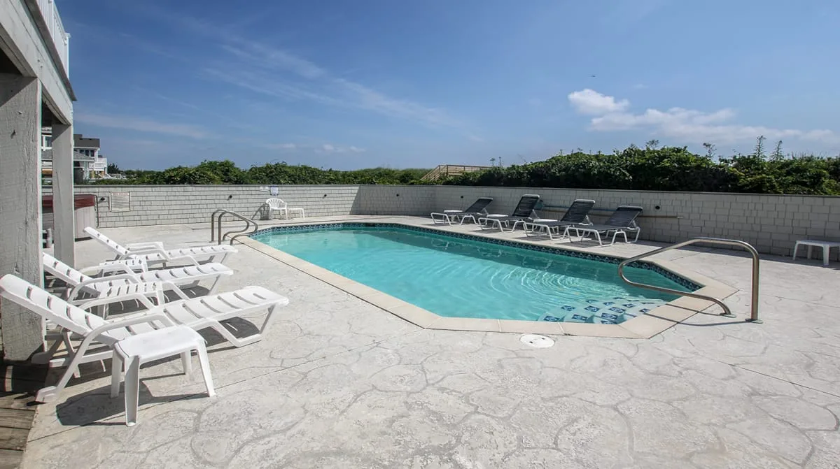 Una piscina al aire libre está rodeada de tumbonas y una terraza pavimentada.