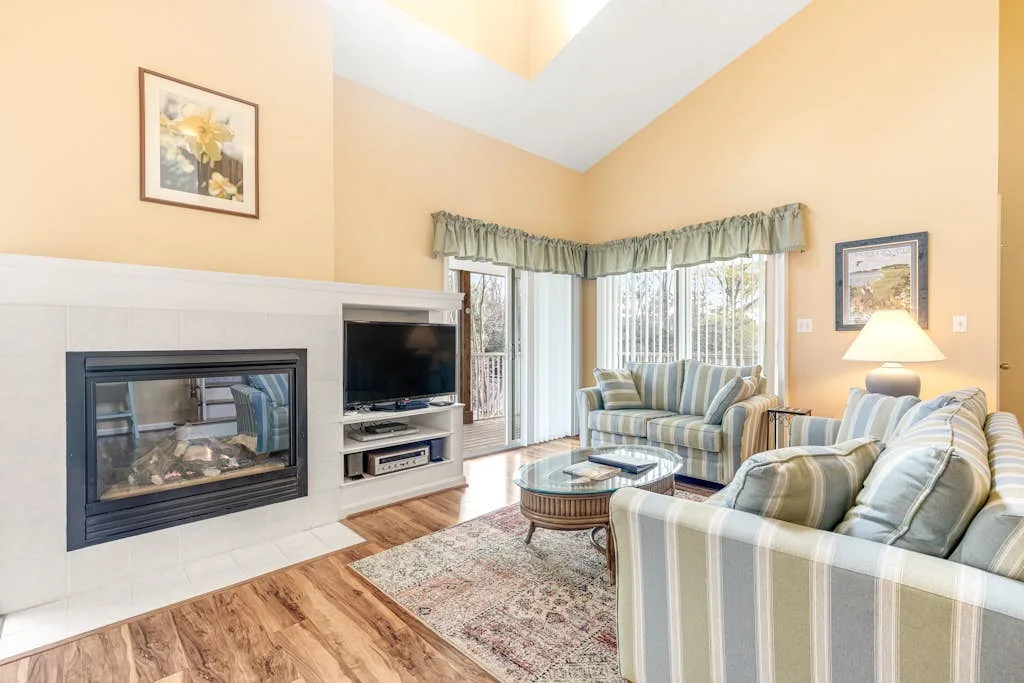 A living room with striped seating, a fireplace, and large windows.