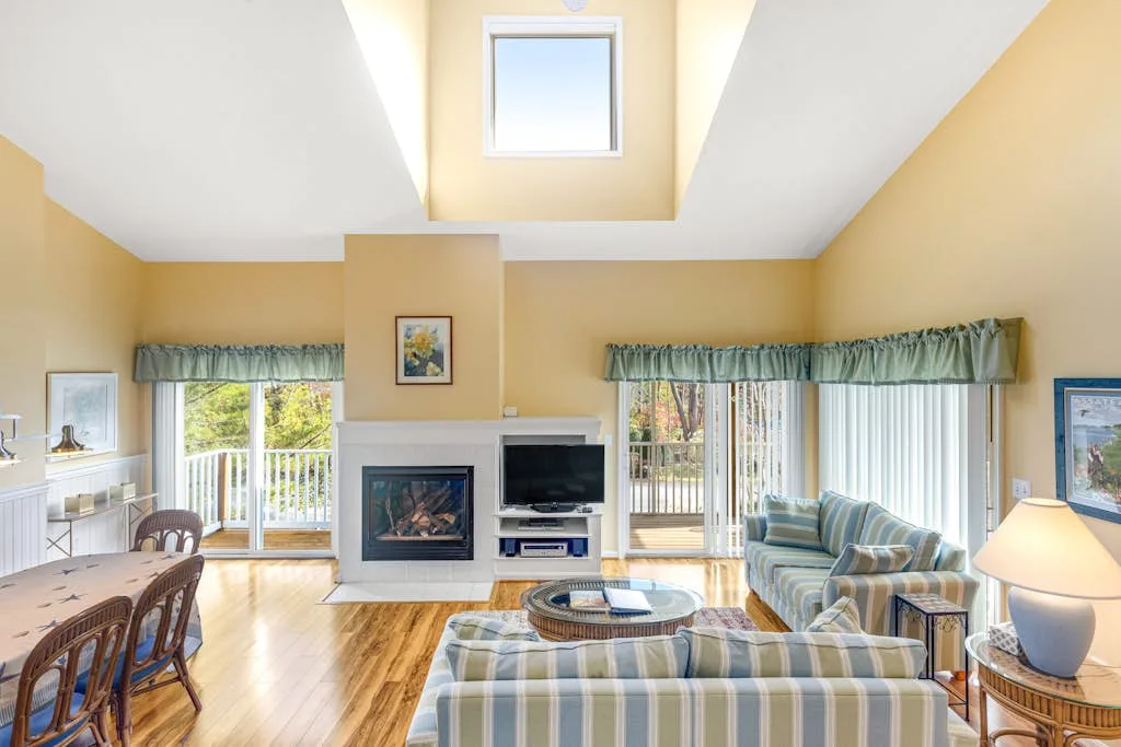 A bright living room with seating, large windows, and a fireplace.