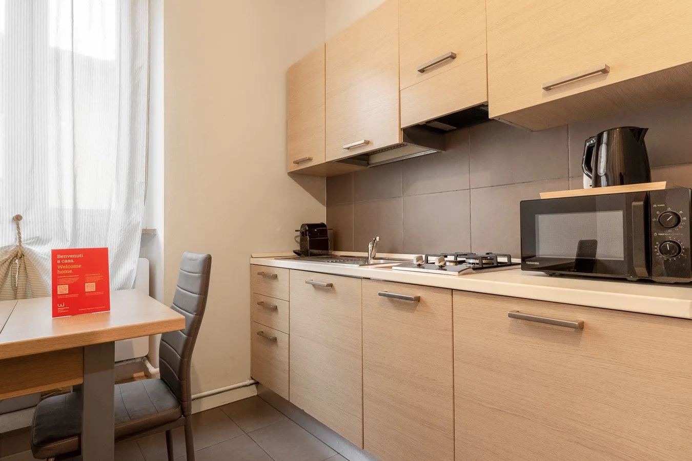 Una cocina luminosa con gabinetes de madera clara, una encimera y una pequeña mesa junto a la ventana.