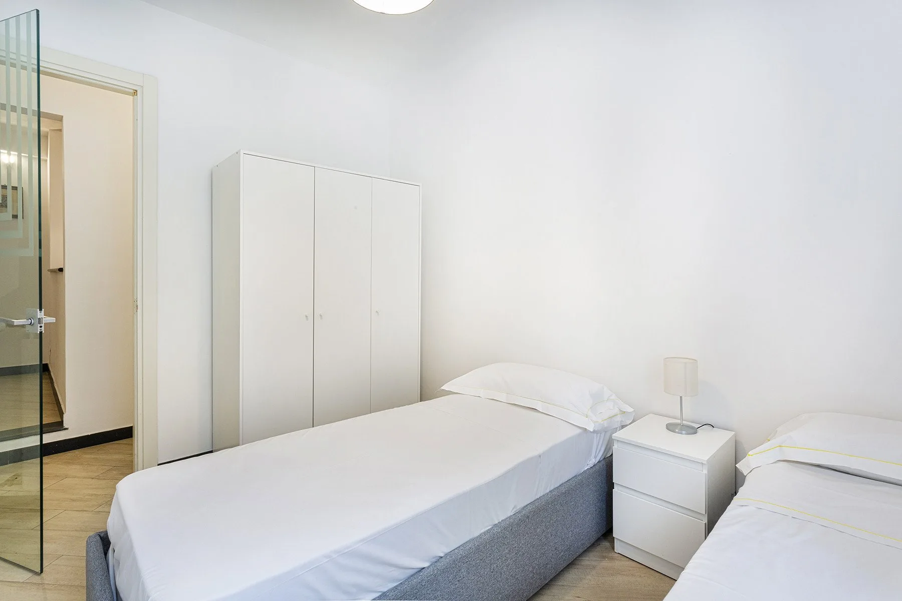 A bright bedroom with two beds, a wardrobe, and a bedside table.