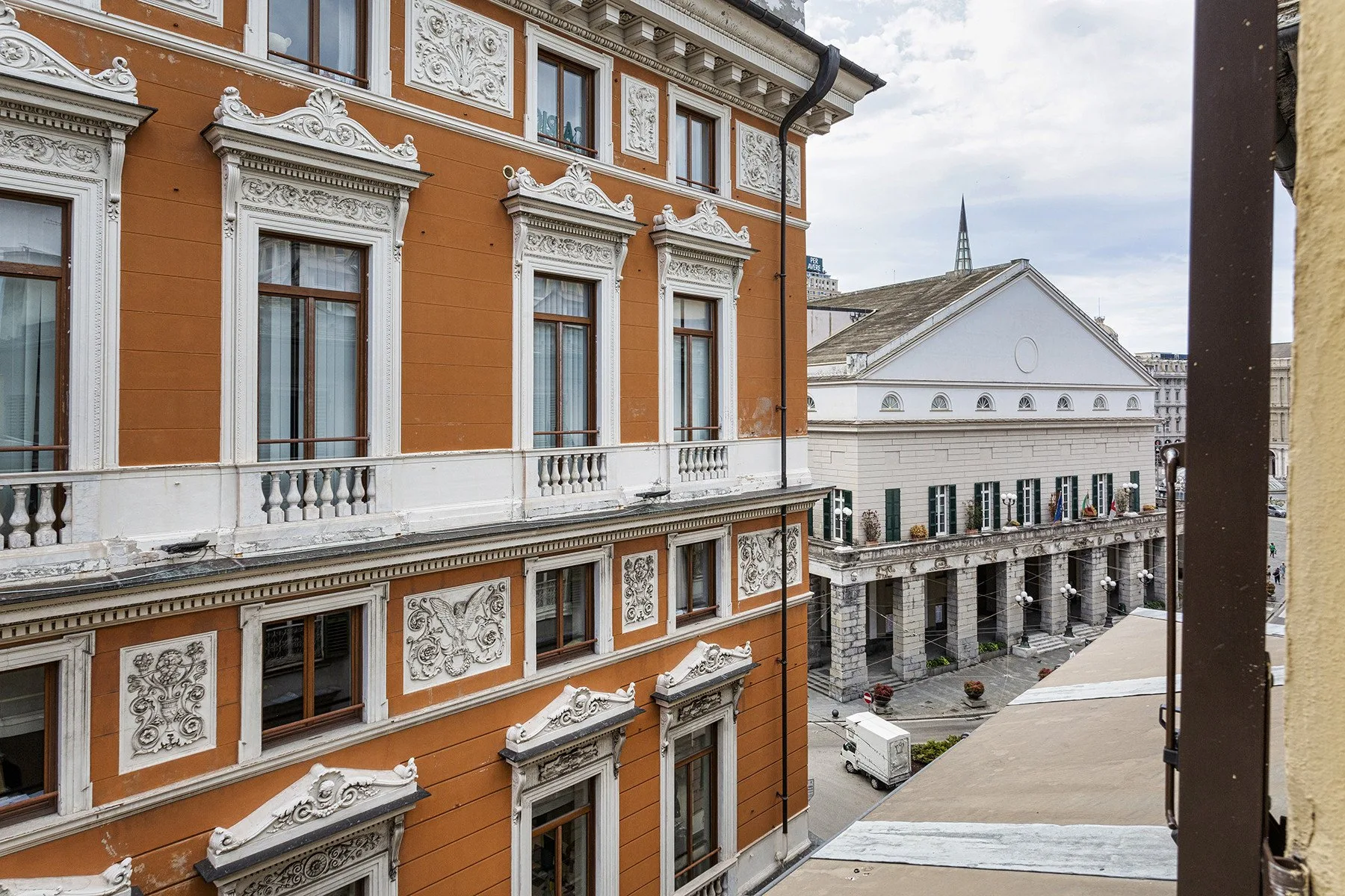 An ornate orange building faces a pale building across a paved courtyard.