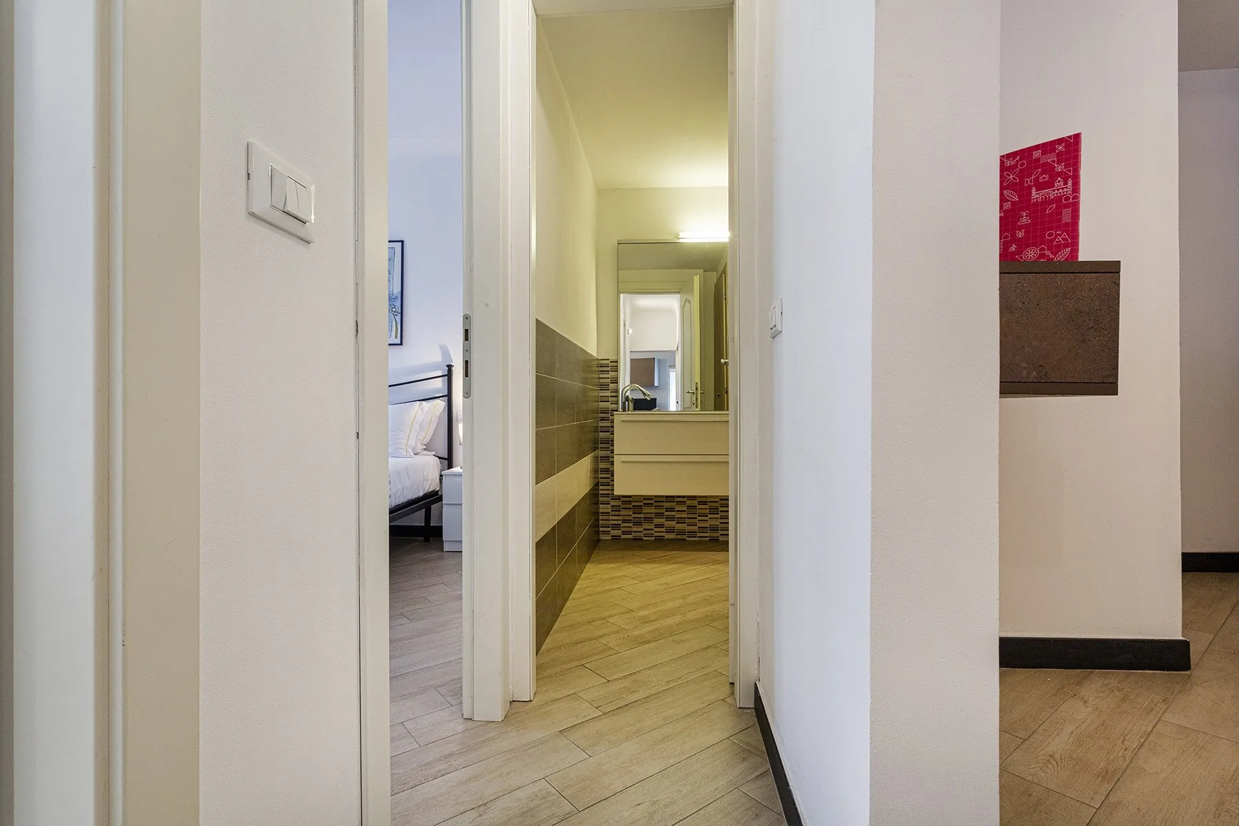 A hallway with tiled flooring leads to a bathroom with a visible sink.