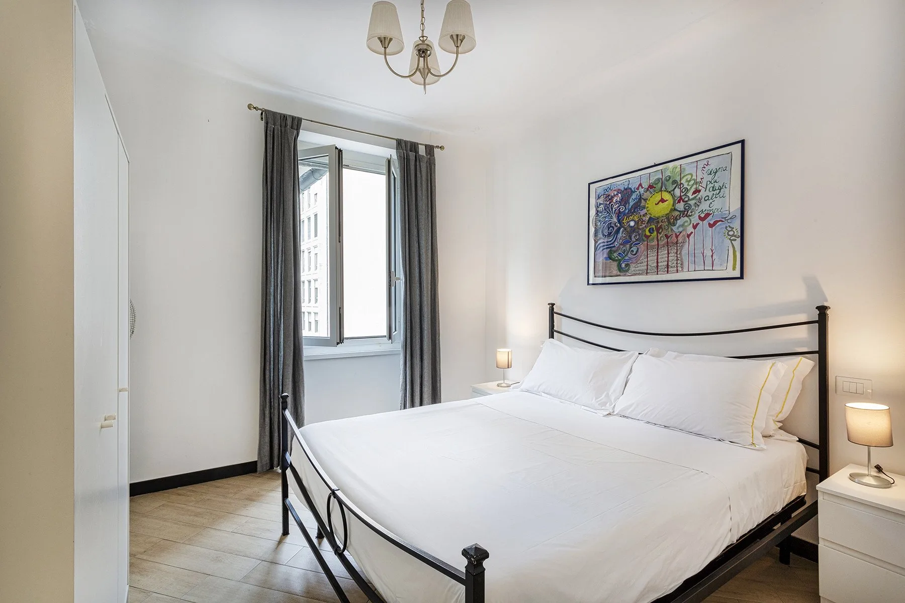 A bright bedroom with a large bed, curtained window, and framed artwork.