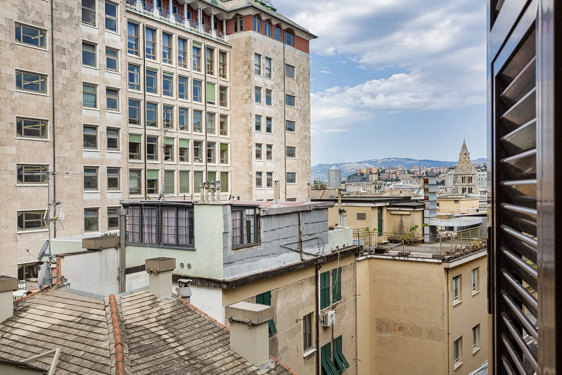 Urban rooftops and nearby buildings are visible beneath a partly cloudy sky.