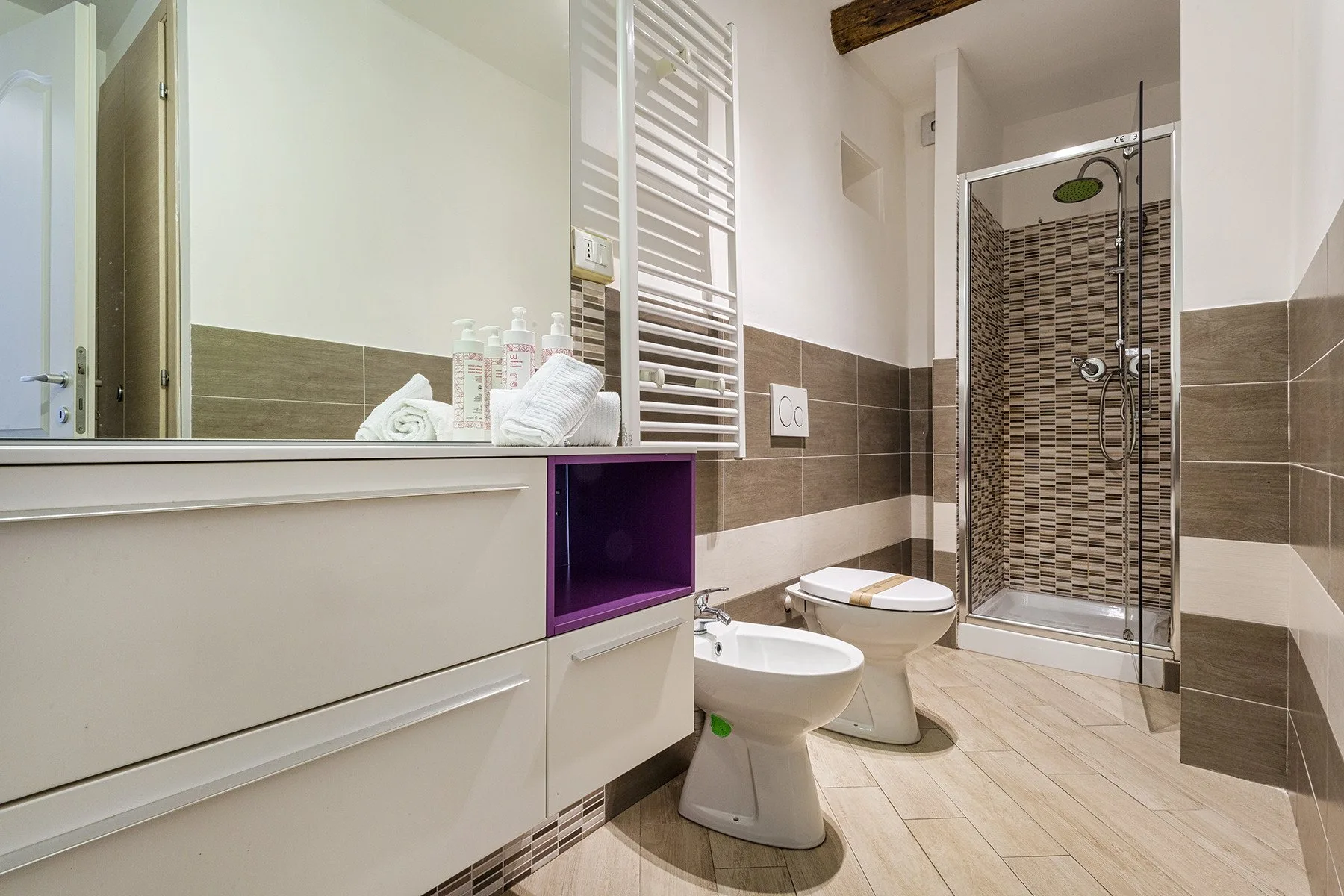 A bathroom with a glass shower, toilet, and sink beneath a wall mirror.