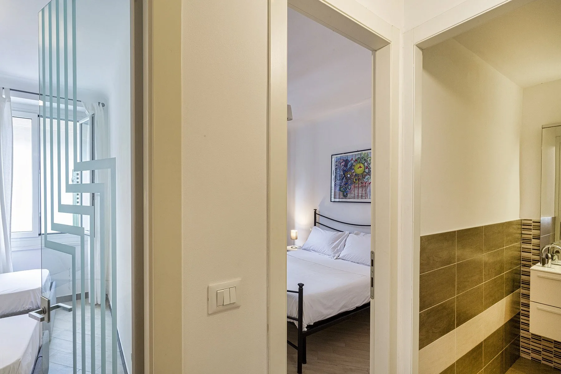 A hallway opens onto a bedroom and a bathroom with tiled walls.