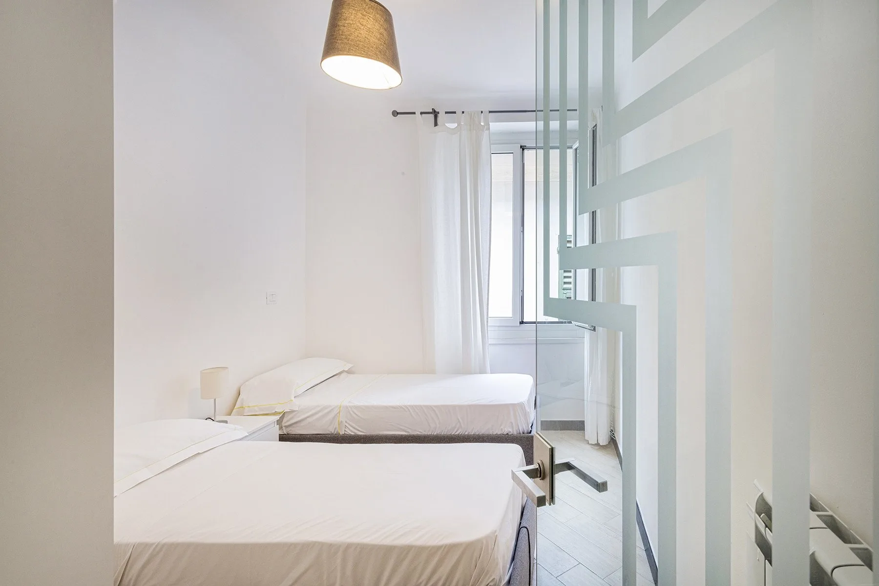 A bright bedroom with two beds and a curtained window.